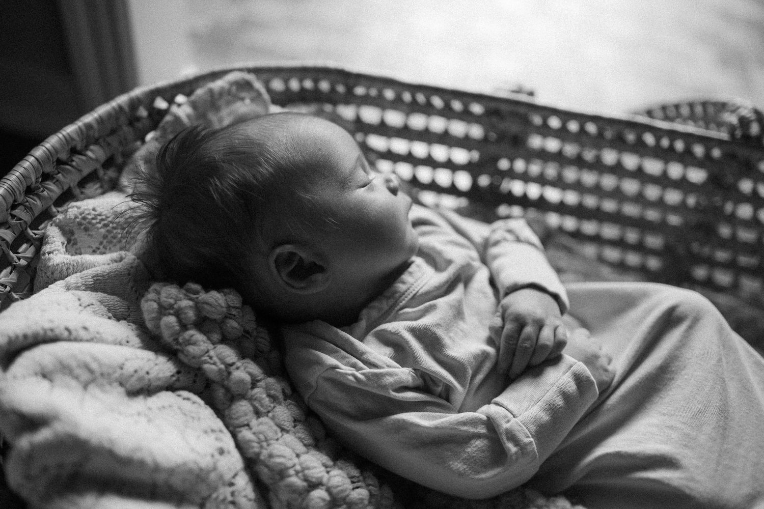 Black and white photo of a baby sleeping peacefully in a wicker chair with blankets.