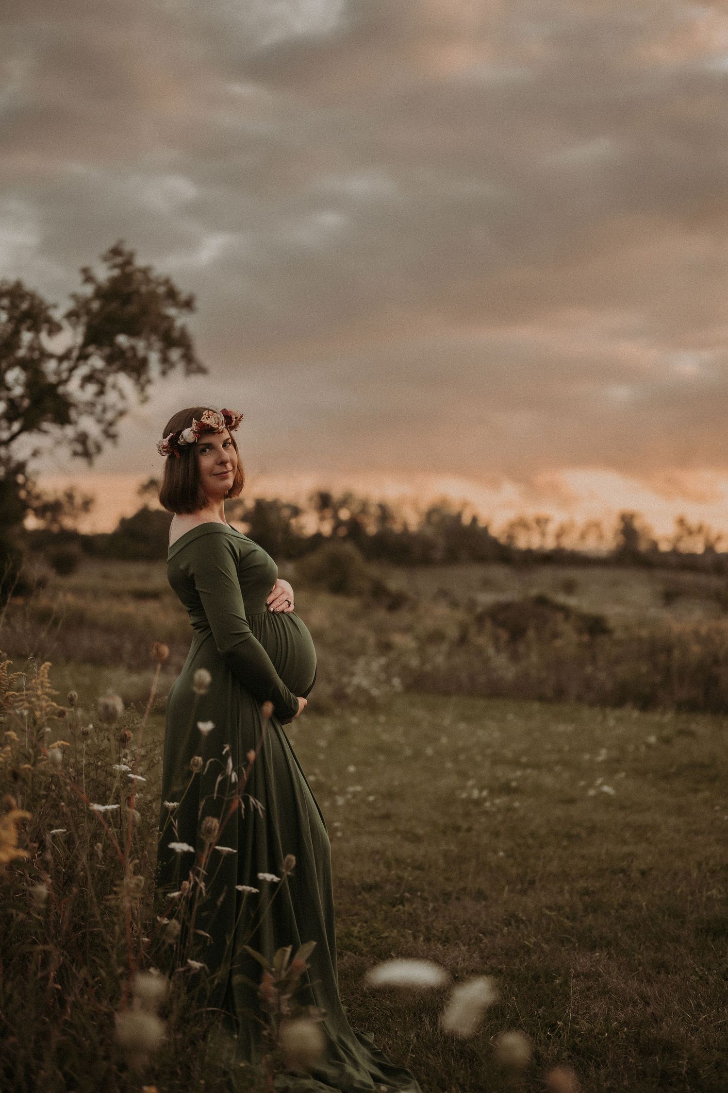Silhouetted against a sunset sky, an expectant mother stands in a flowing green dress.