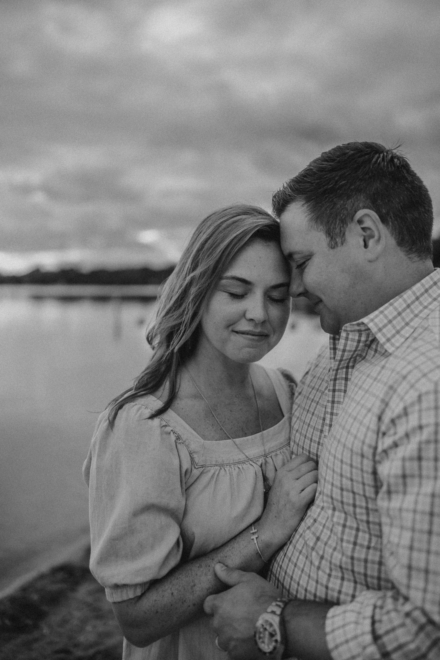 An intimate black and white portrait of a couple on a cloudy beach.