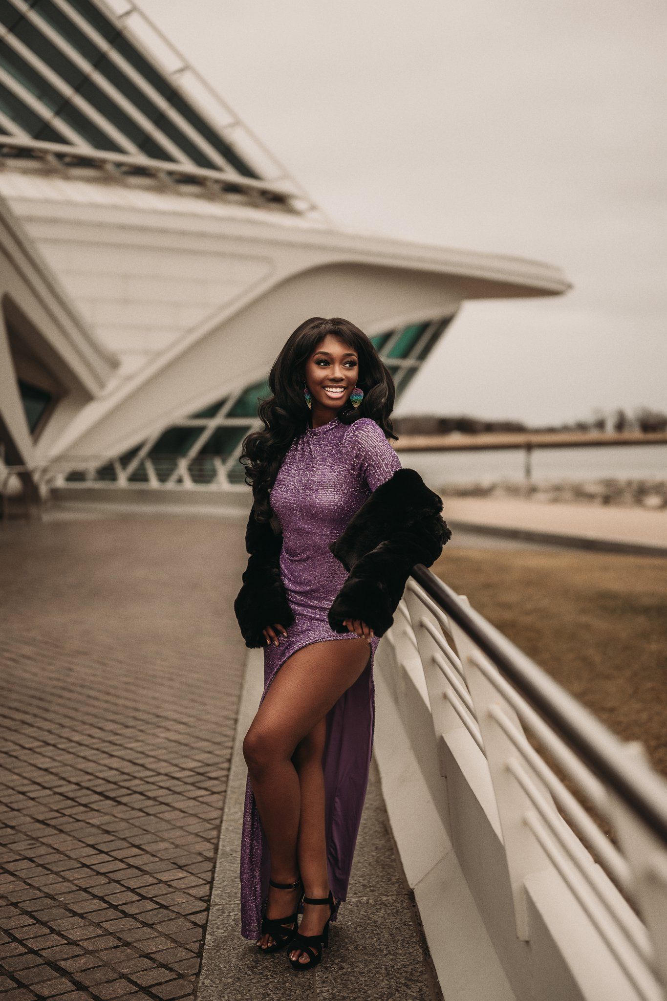 Glamorous fashion photo featuring a purple sequin dress and black fur coat against modern architecture background.
