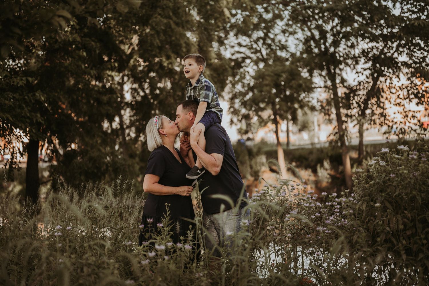 Family shares playful moment together while standing in wildflower field at dusk.