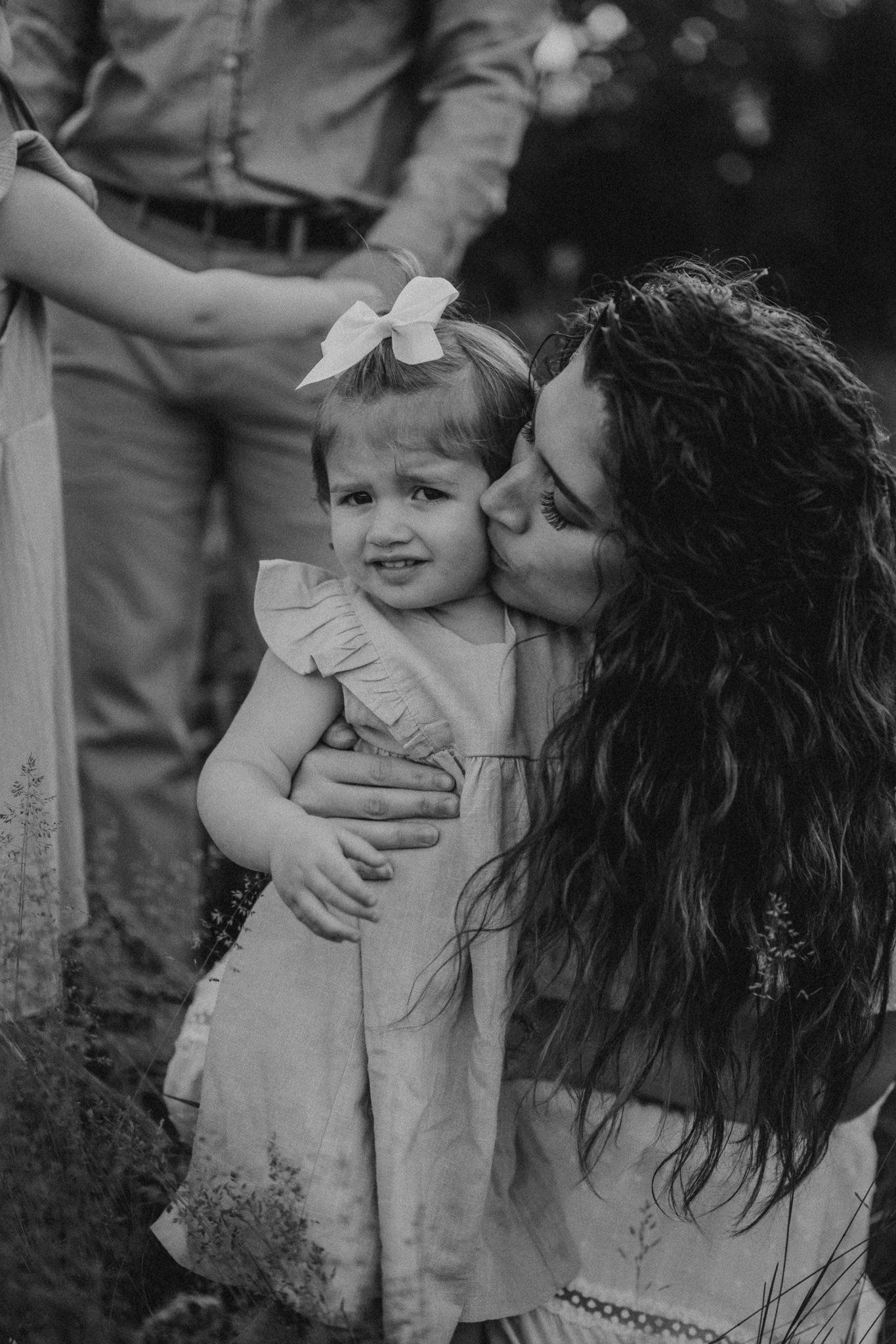 Intimate black and white portrait showing tender moment between parent and child in outdoor setting.