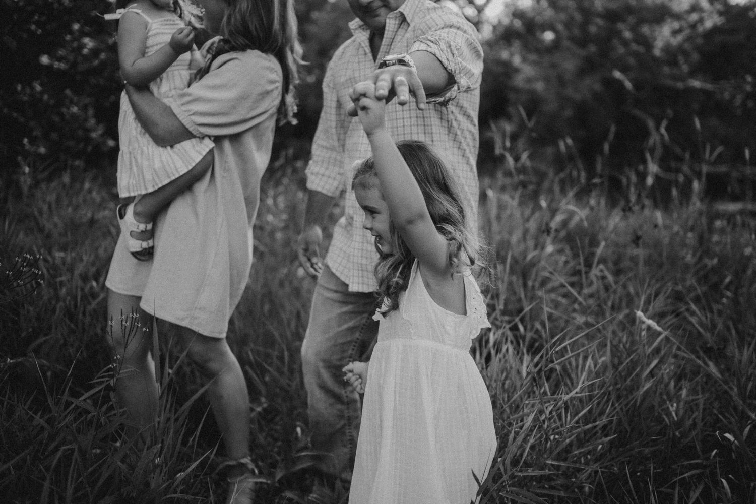 A black and white portrait of a family sharing playful moments in tall grass.
