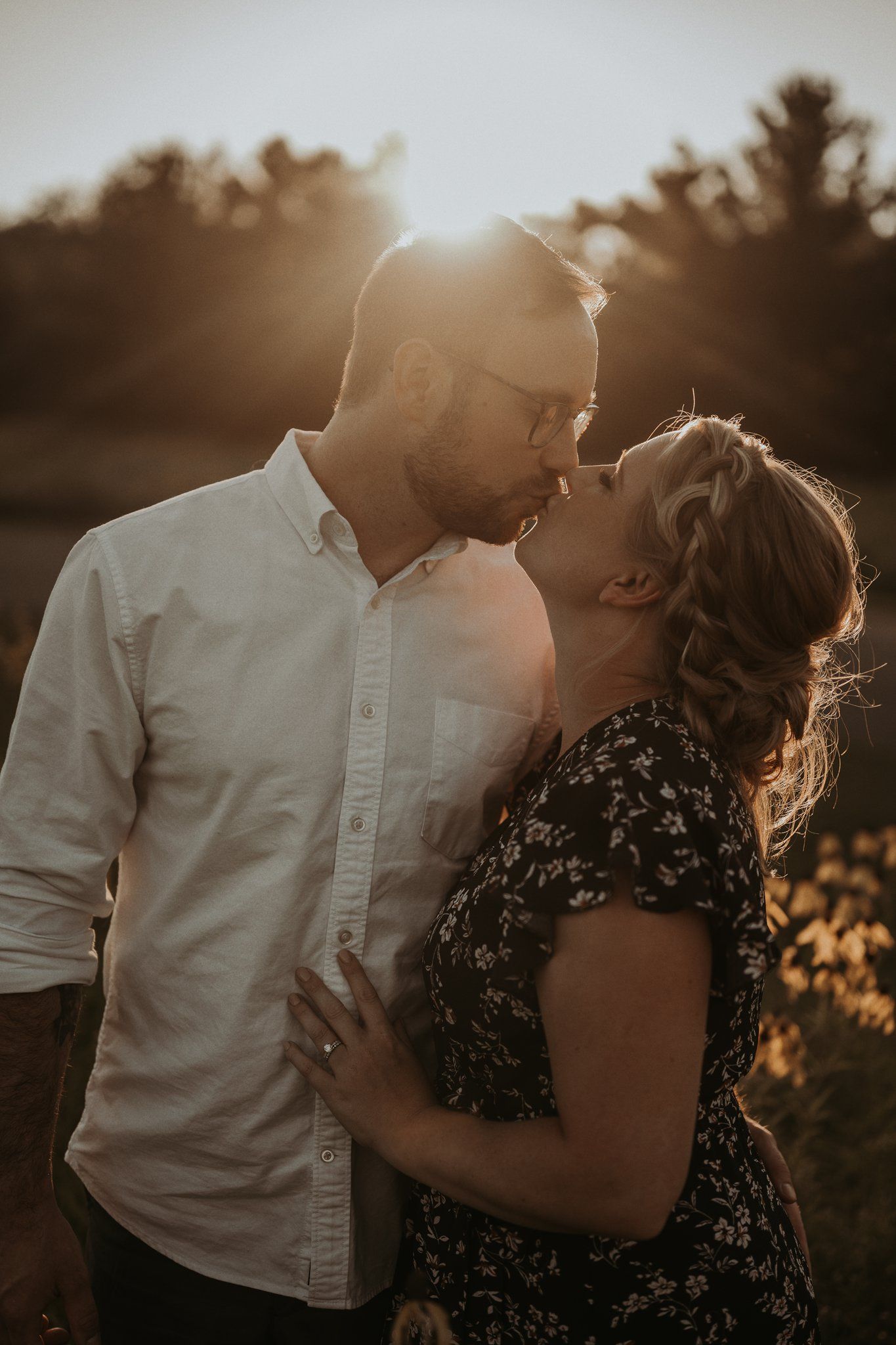 Romantic couple embracing in a sunlit wildflower field during golden hour sunset.