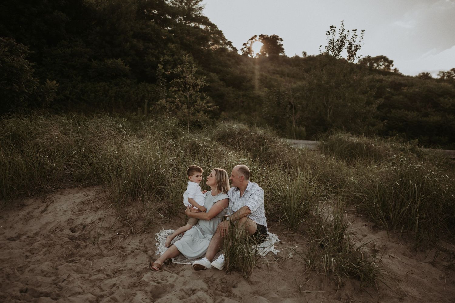 Family sits together on hillside during moody sunset photoshoot.