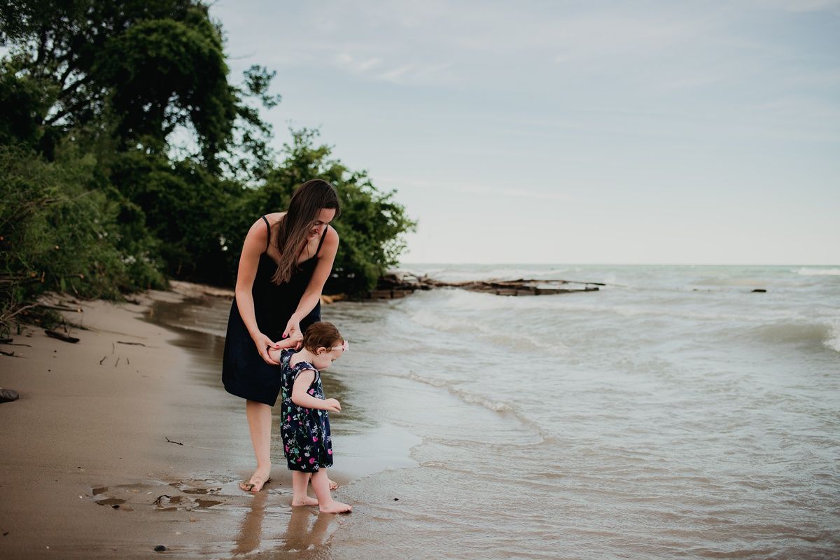 A parent and child hold hands while walking along a natural beach shoreline.