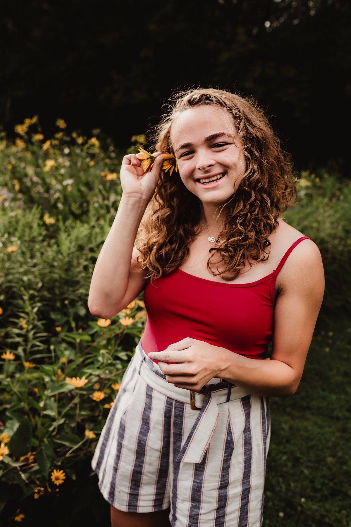 Summer outdoor portrait among yellow flowers wearing red tank top and striped shorts.