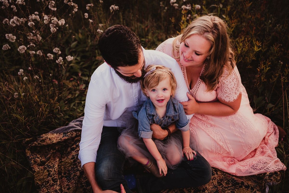 Family sitting together outdoors with pink dress and white shirt against blooming flowers at sunset.