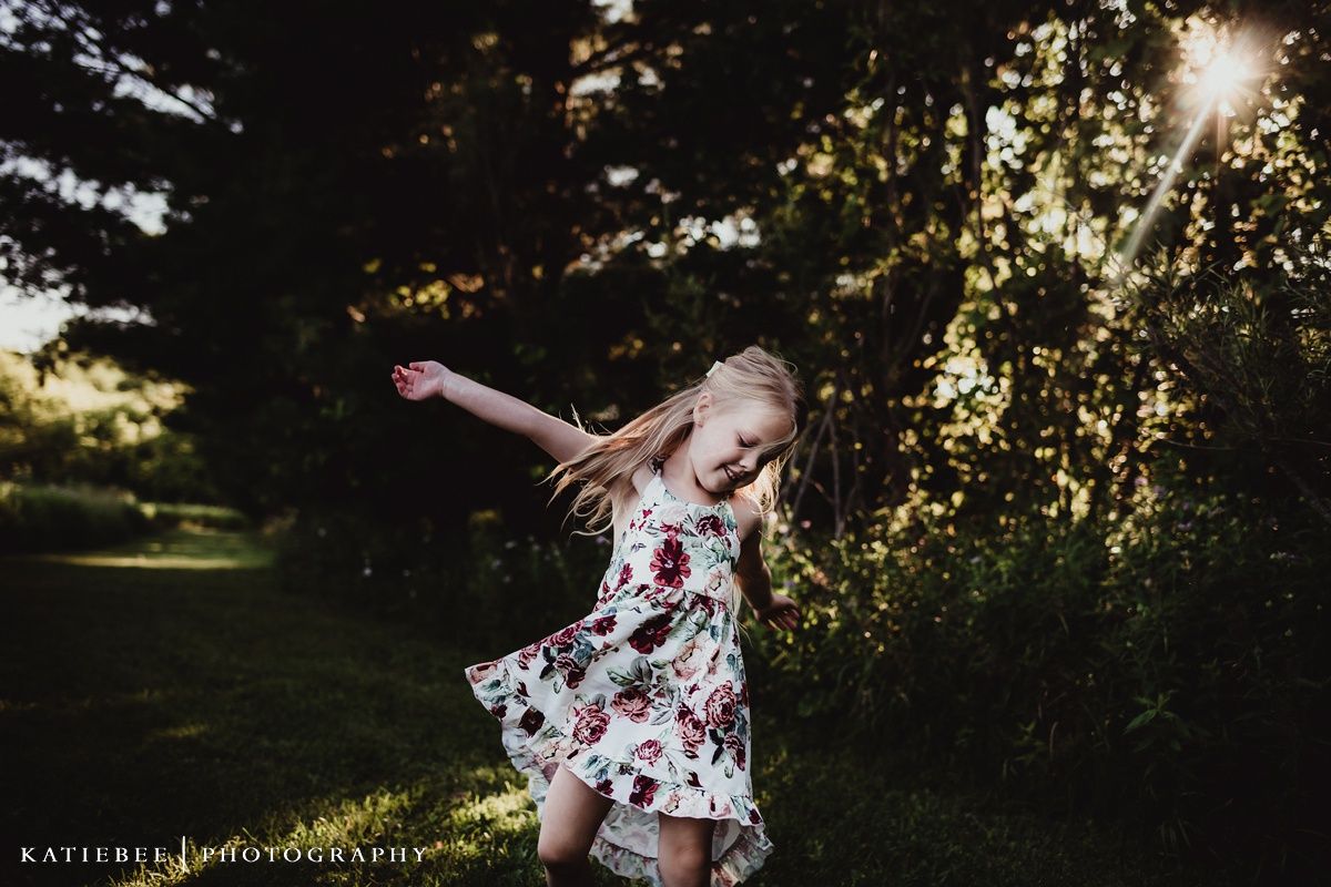 Young child in floral dress twirling joyfully at sunset in a garden setting.