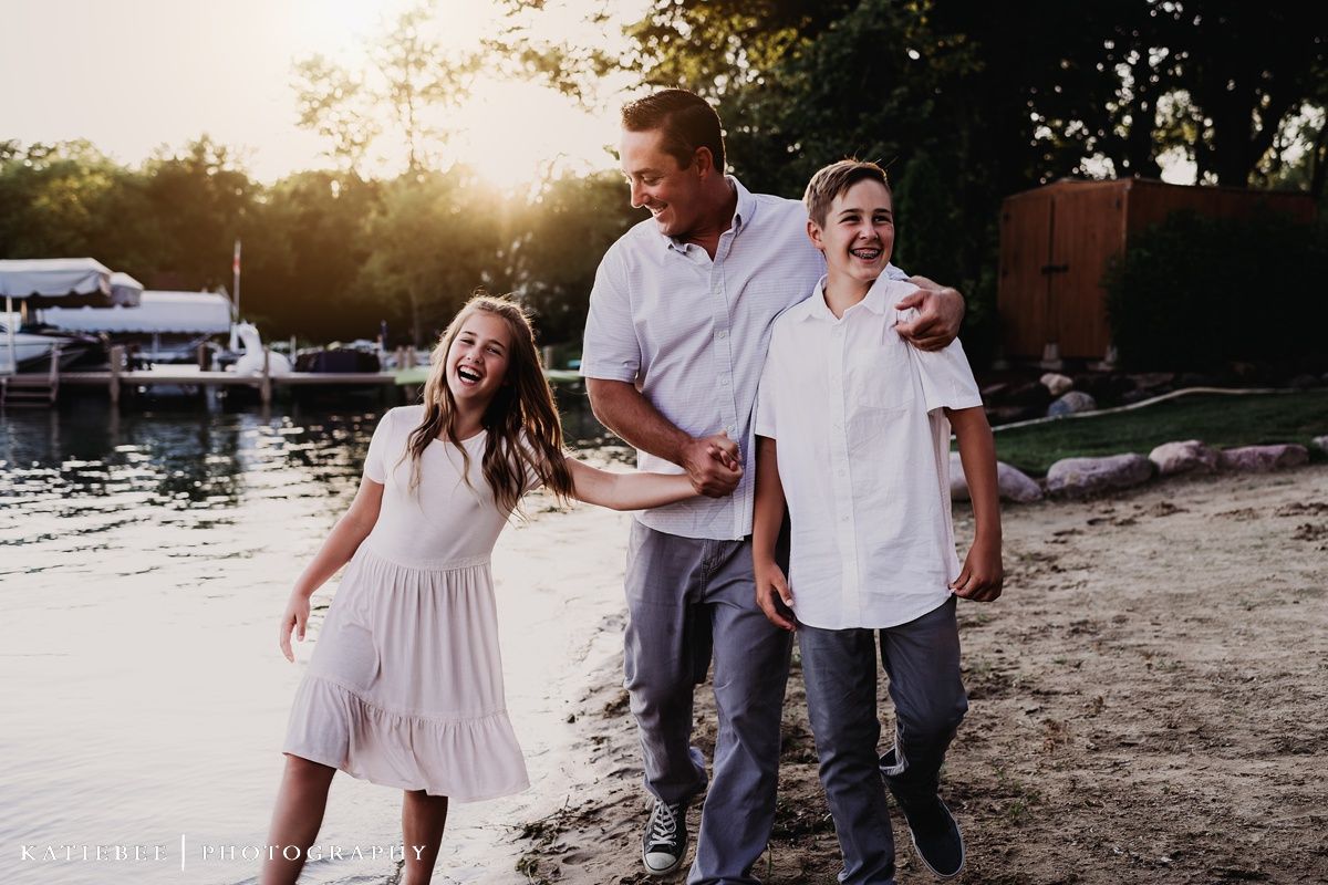 A family walks together along a waterfront beach at sunset.