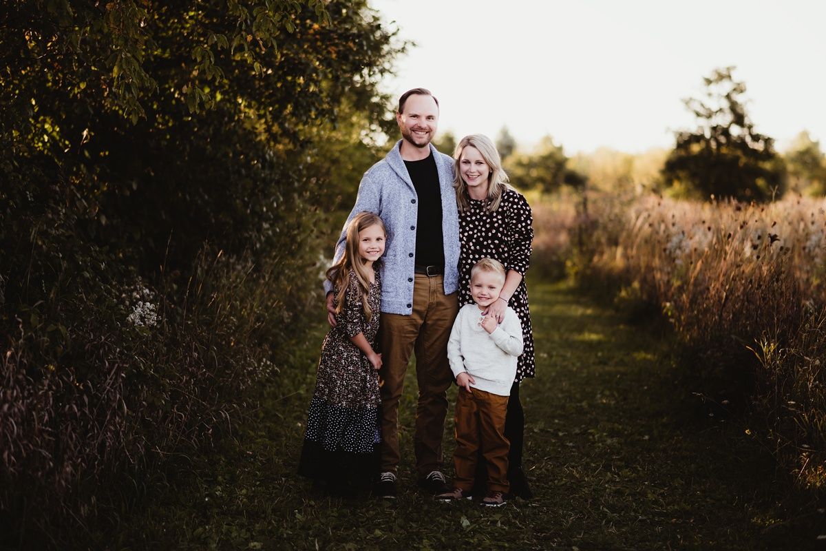 Family of four poses together on nature path during golden hour.