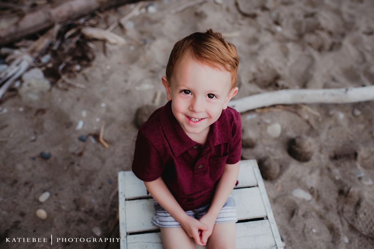 A child in a burgundy shirt sits on white furniture outdoors.
