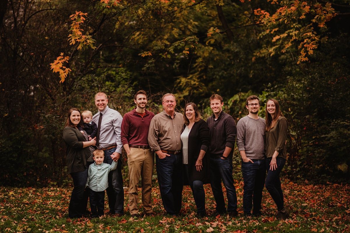 Large family group portrait in autumn setting with colorful fall foliage in background.