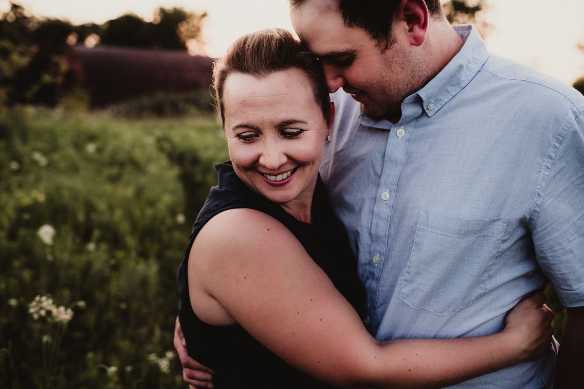 A couple shares a tender embrace while laughing in a summer meadow during sunset.