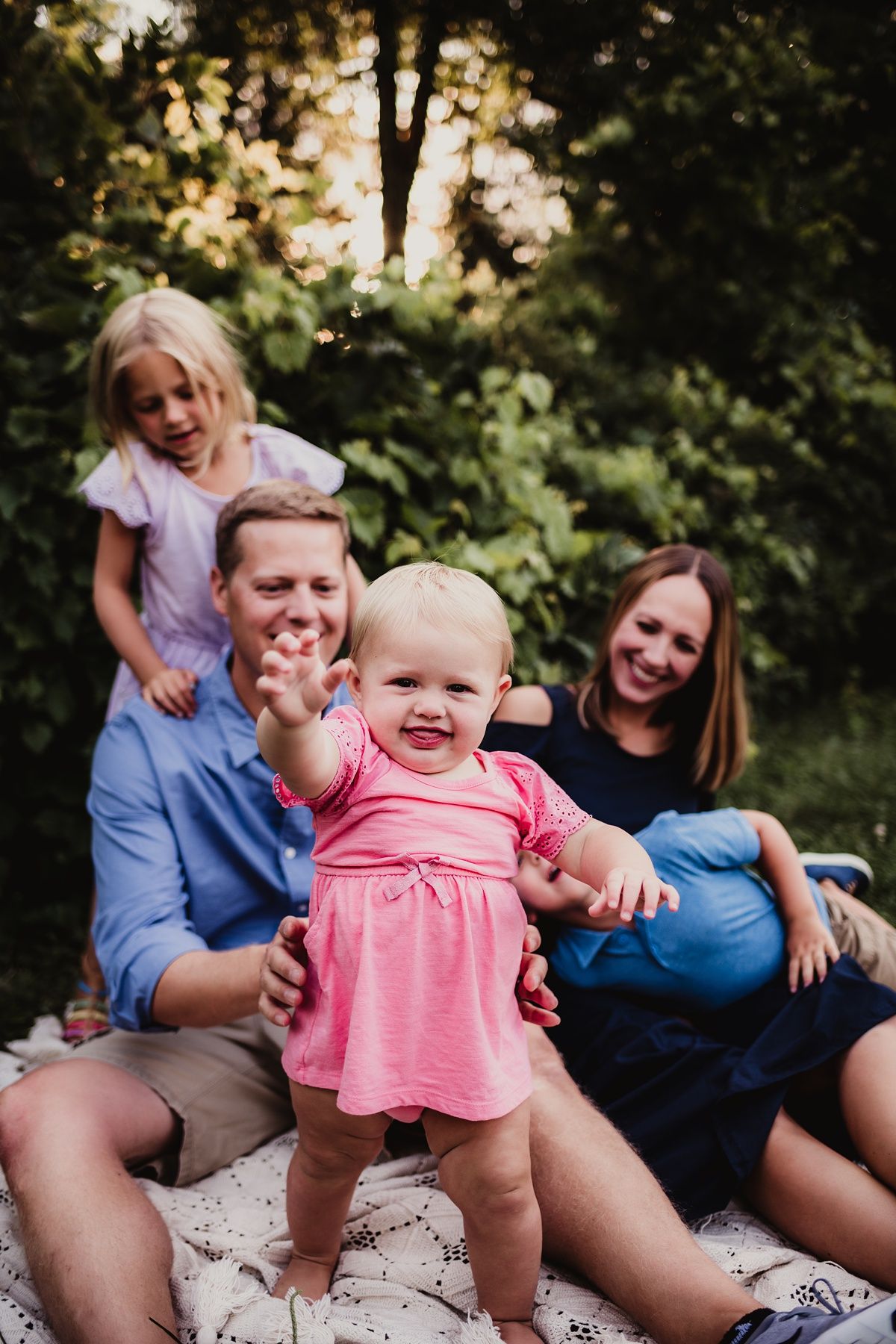 Happy family sitting together outdoors while toddler in pink dress dances.