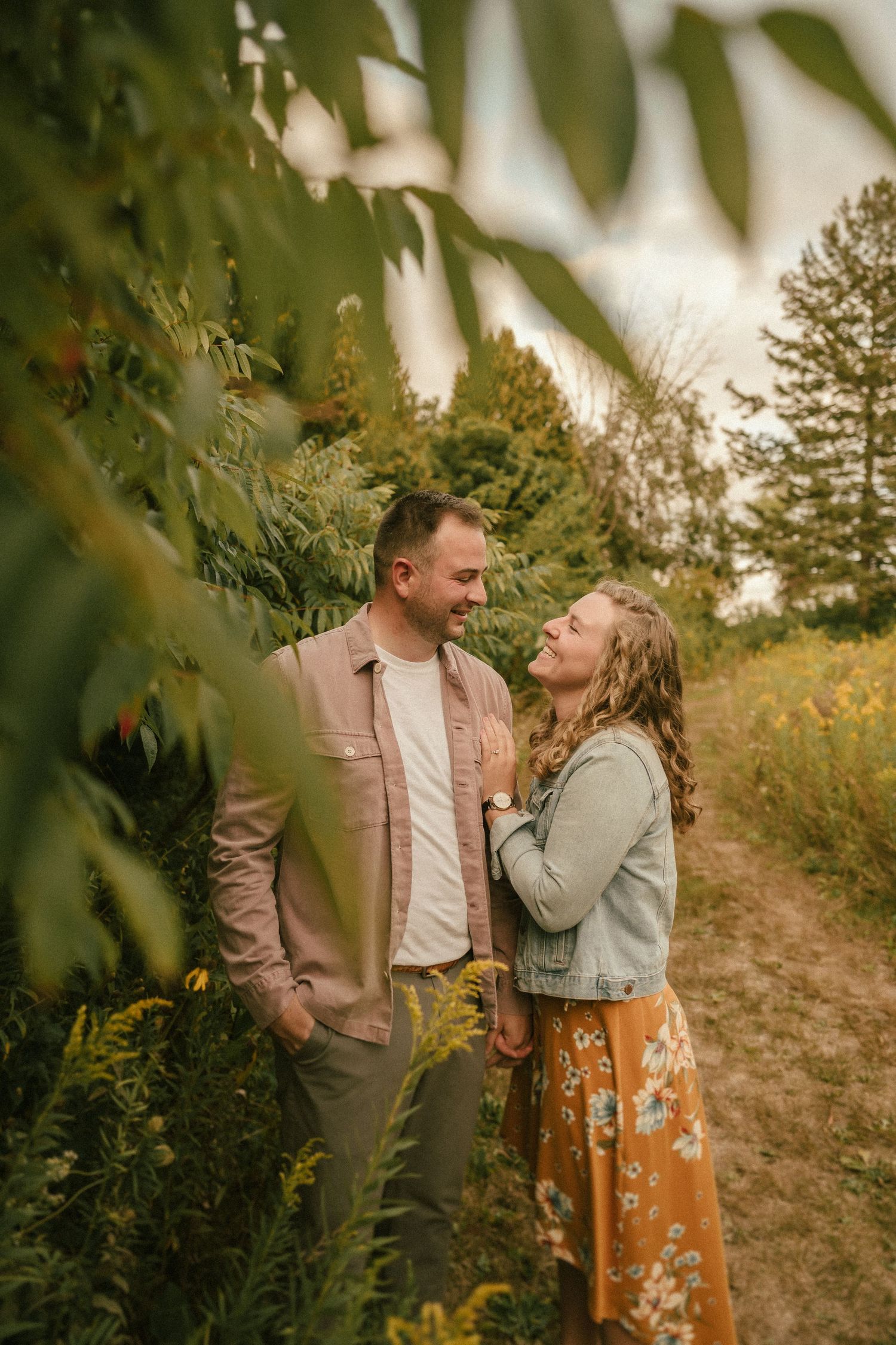 Two people share laughter on a scenic path framed by leaves and warm autumn light.