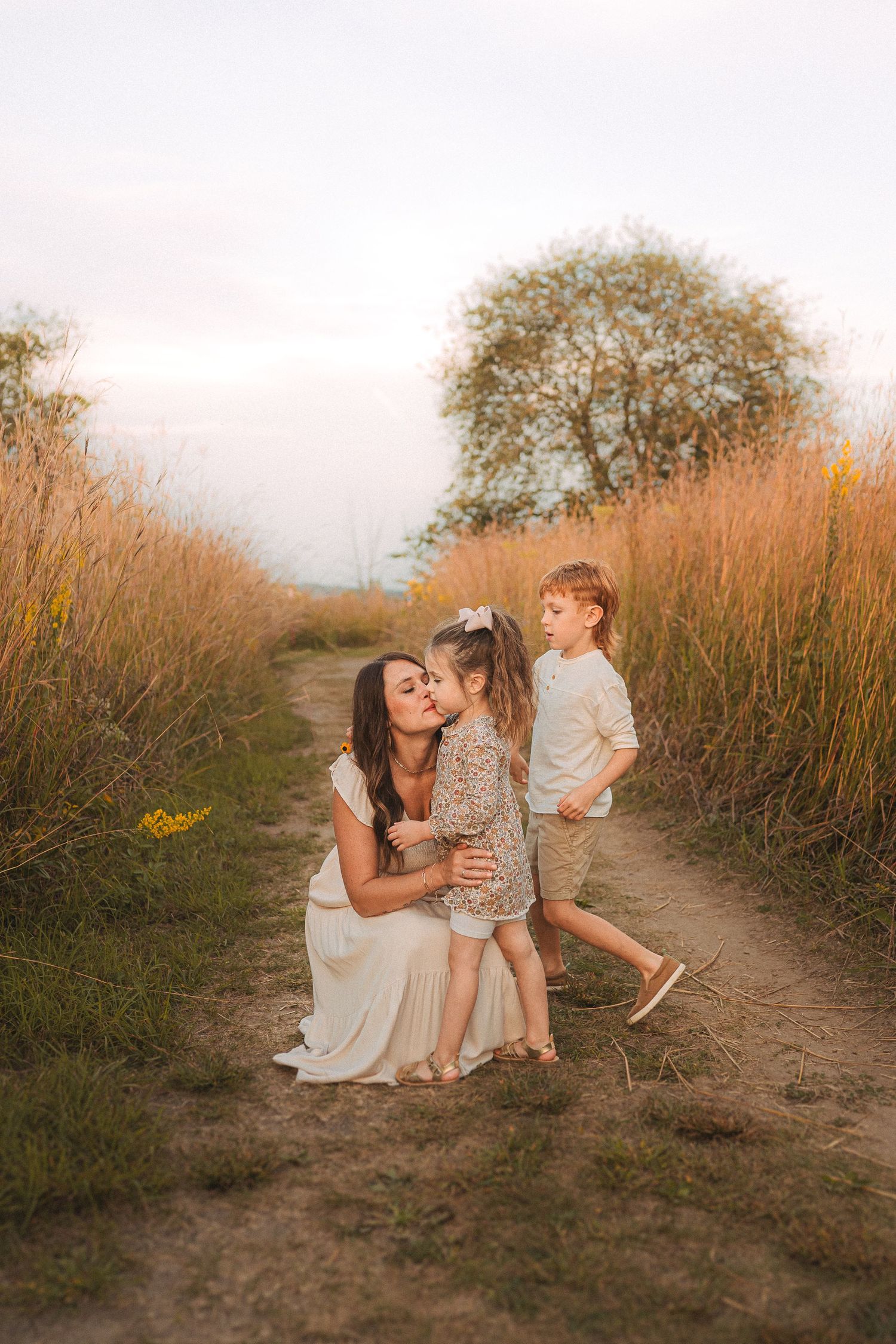 Candid family photo on dirt path with golden grass and sunset sky backdrop.