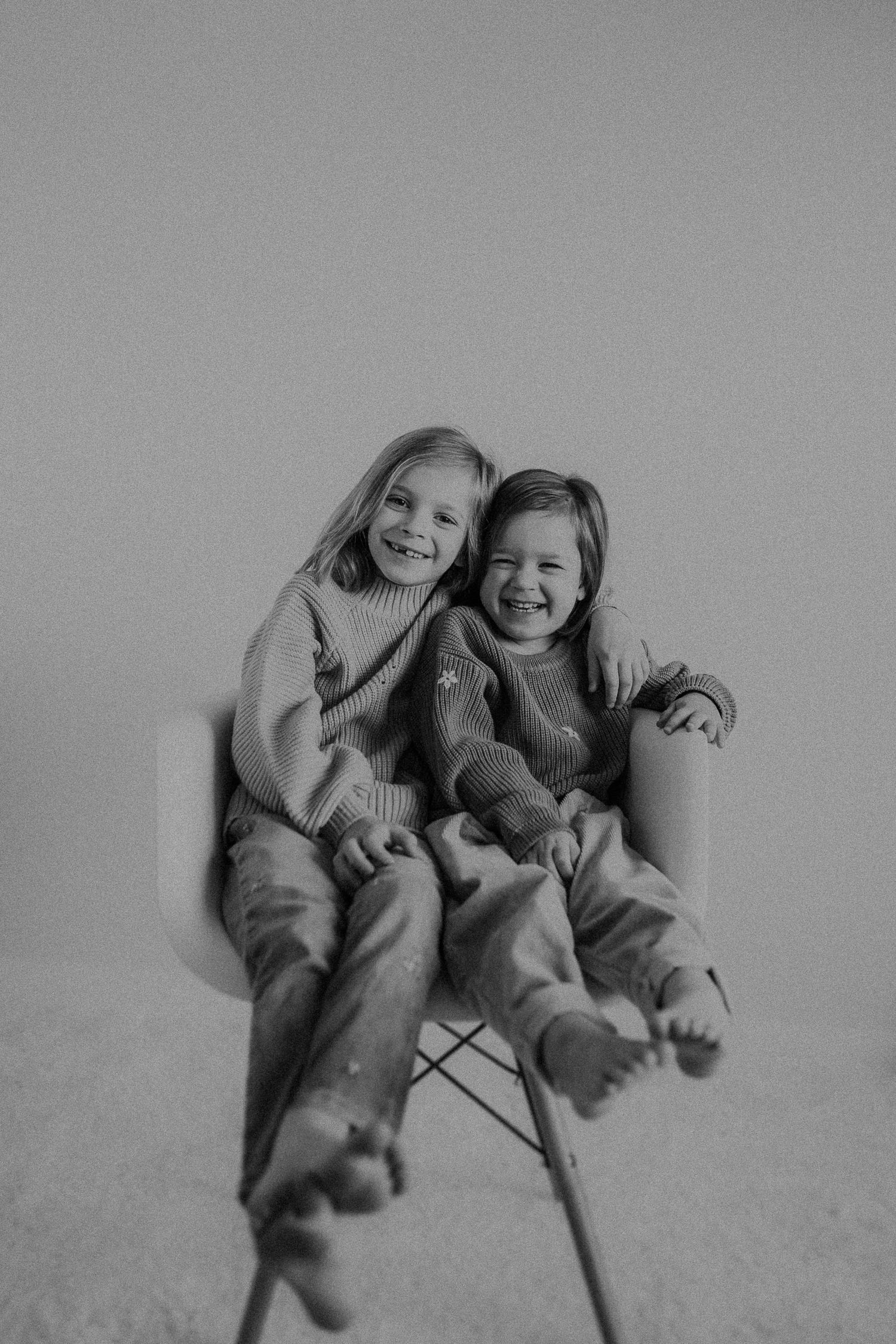 Two children sitting together in matching sweaters on a modern chair.