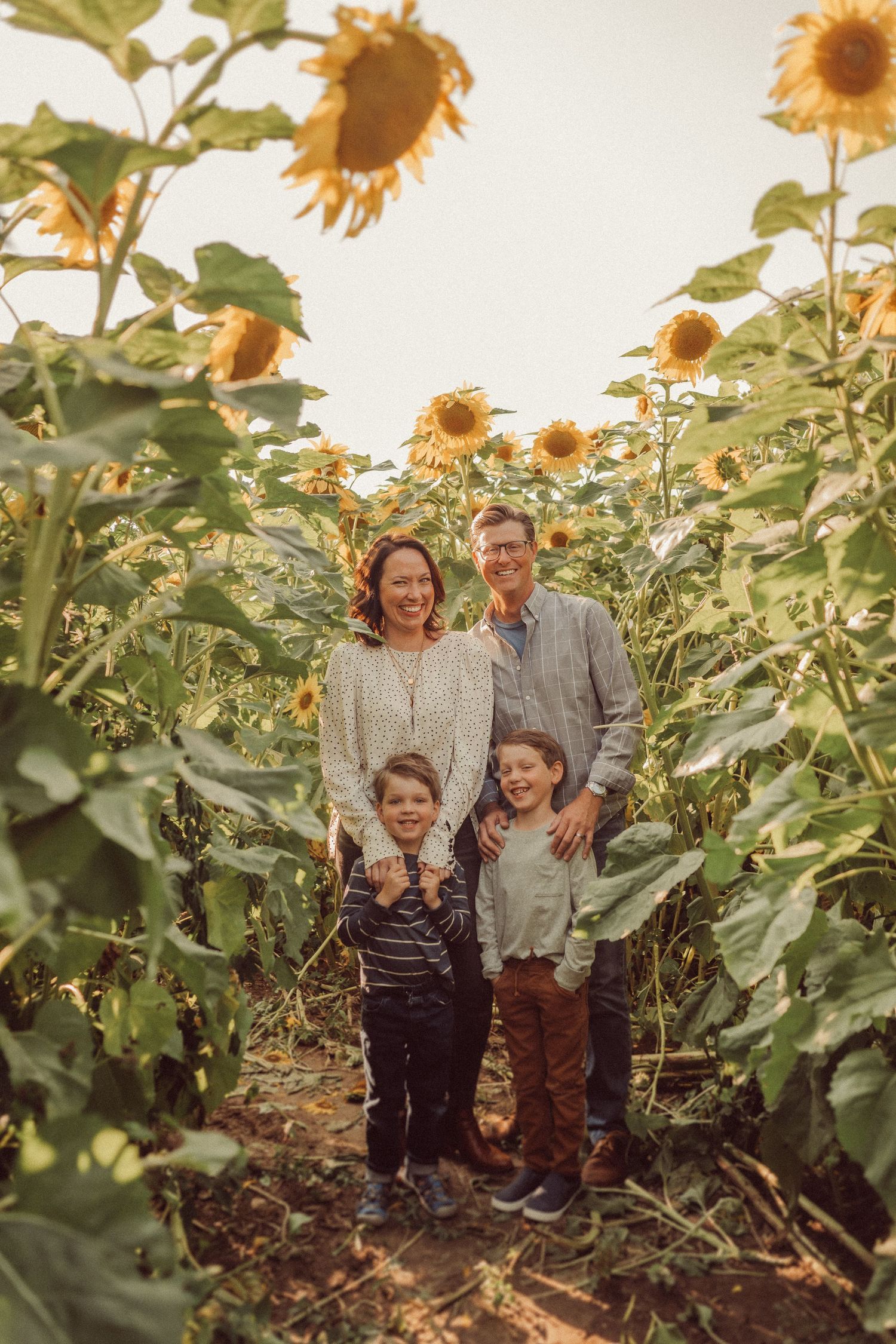 Family portrait taken in a sunflower field during golden hour.