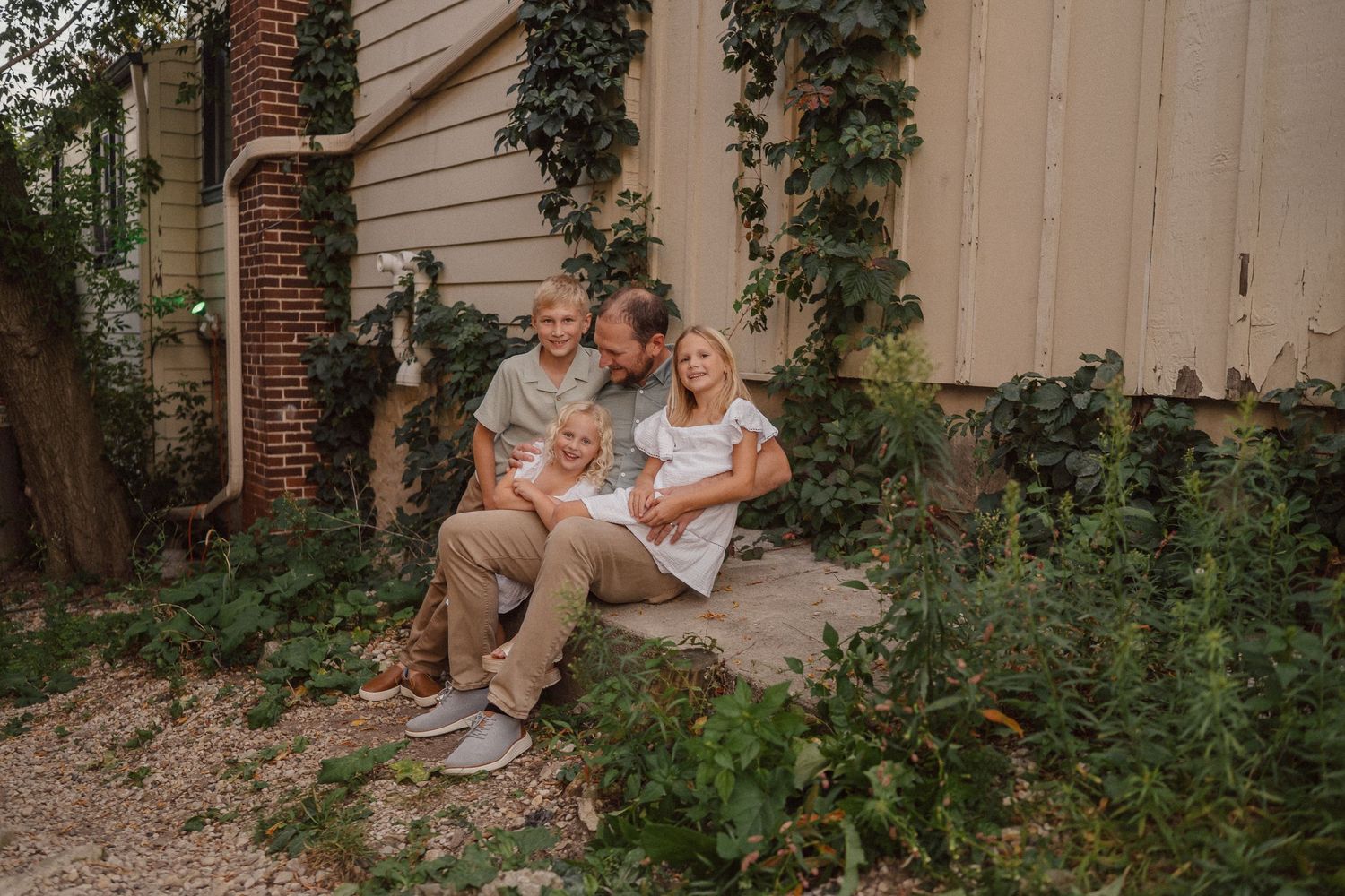 A couple sits together on stone steps surrounded by lush green ivy and brick columns in a romantic garden setting.