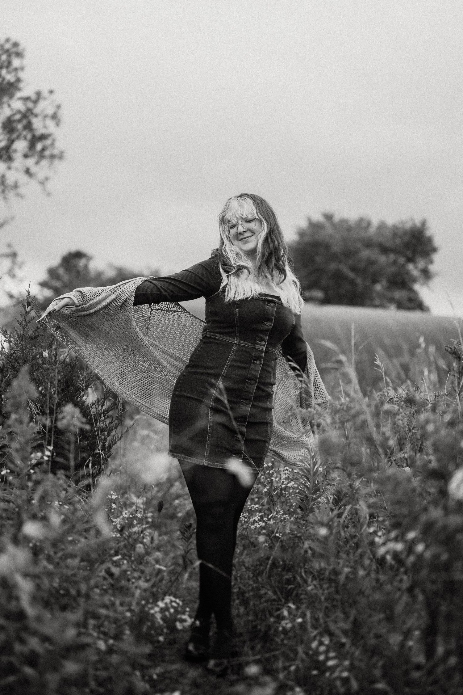 Black and white portrait in flowing dress among wild grasses and flowers.