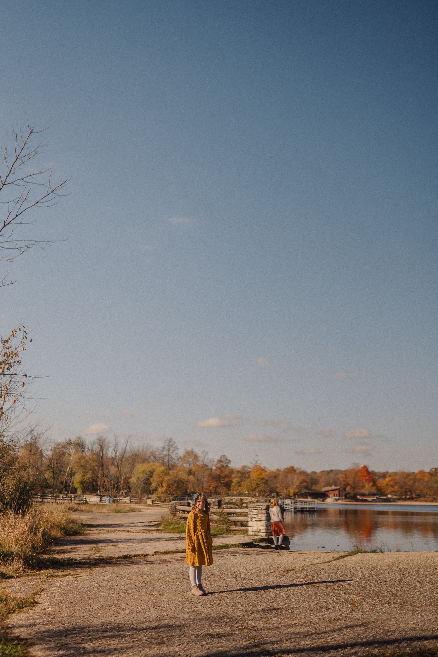 A scenic lakeside beach view with fall foliage and people walking along the shoreline.