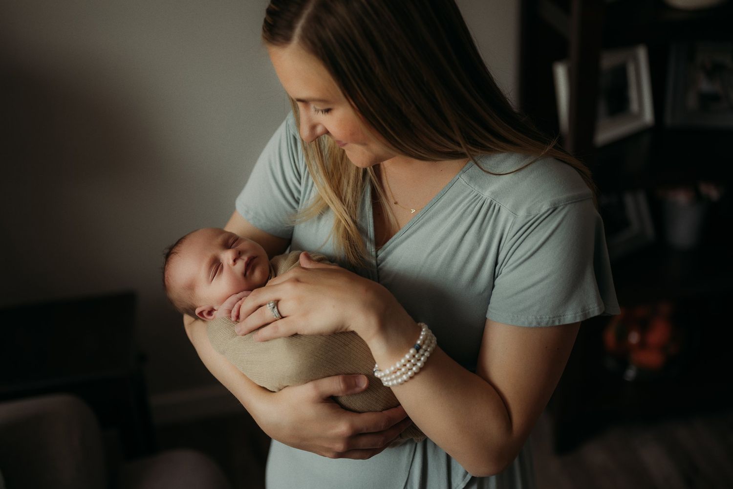Parent in blue dress tenderly holding newborn baby in dimly lit room.