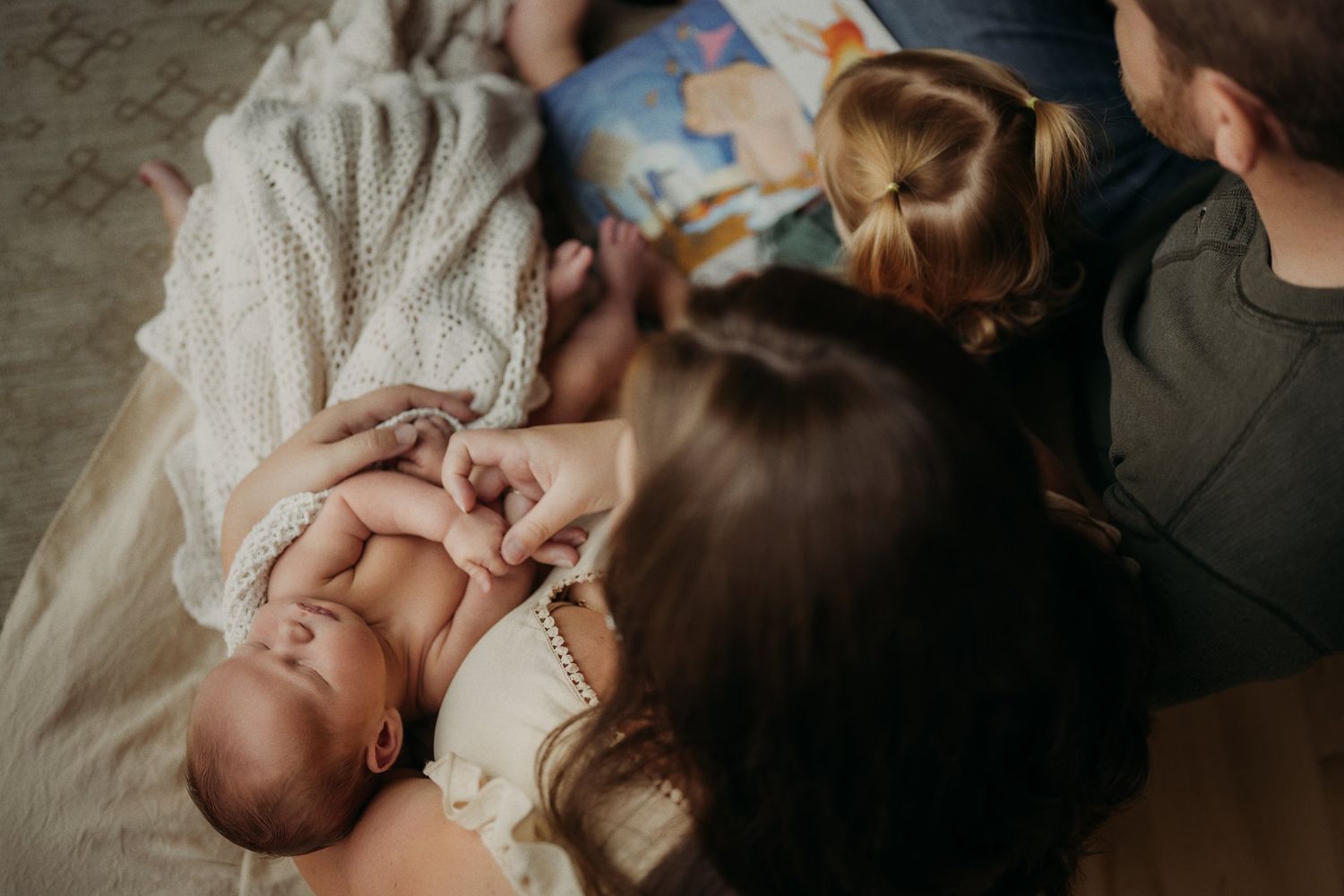Intimate family moment with infant lying on soft blanket surrounded by loved ones.