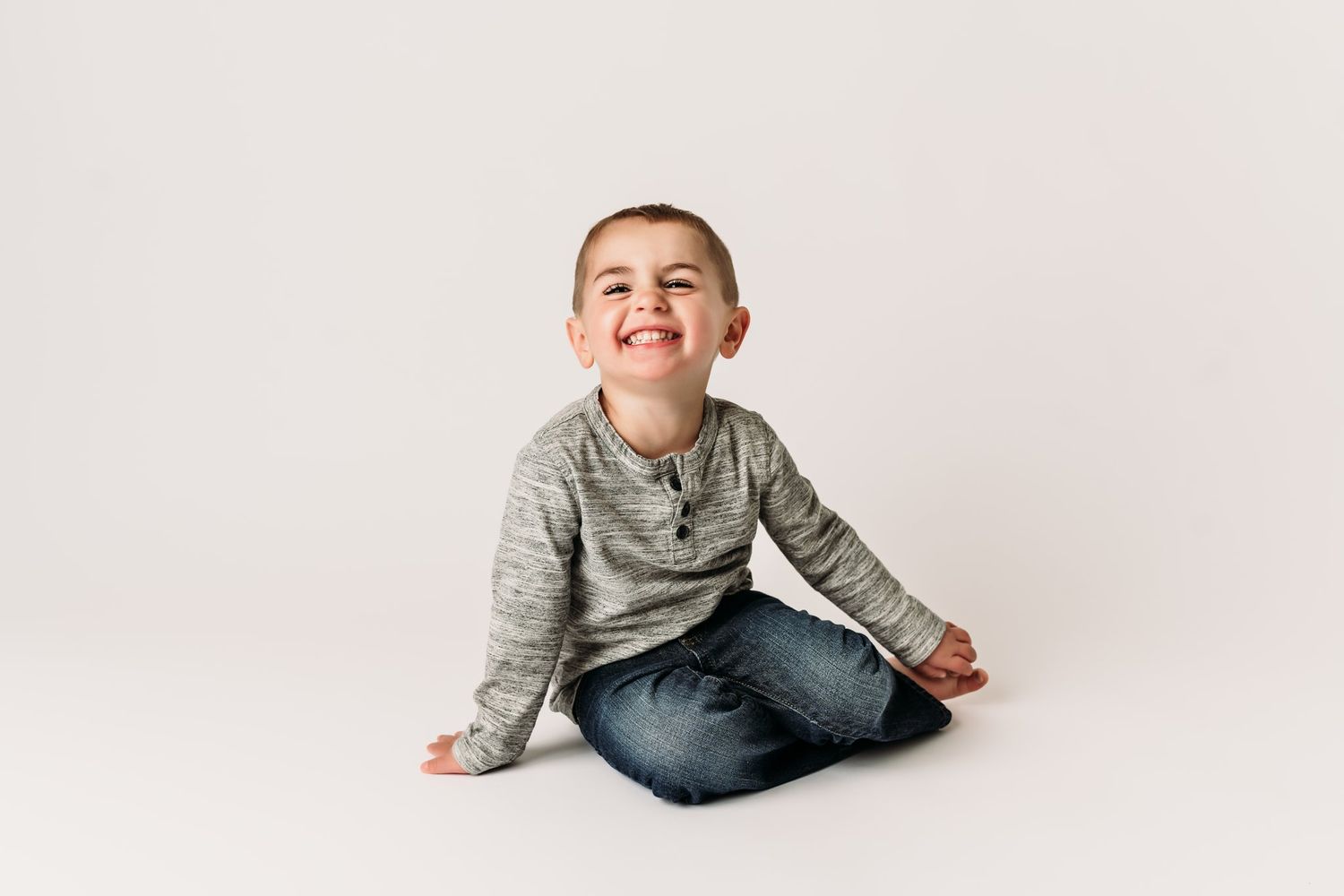 A candid sitting portrait on white background showing joyful expression in casual attire.
