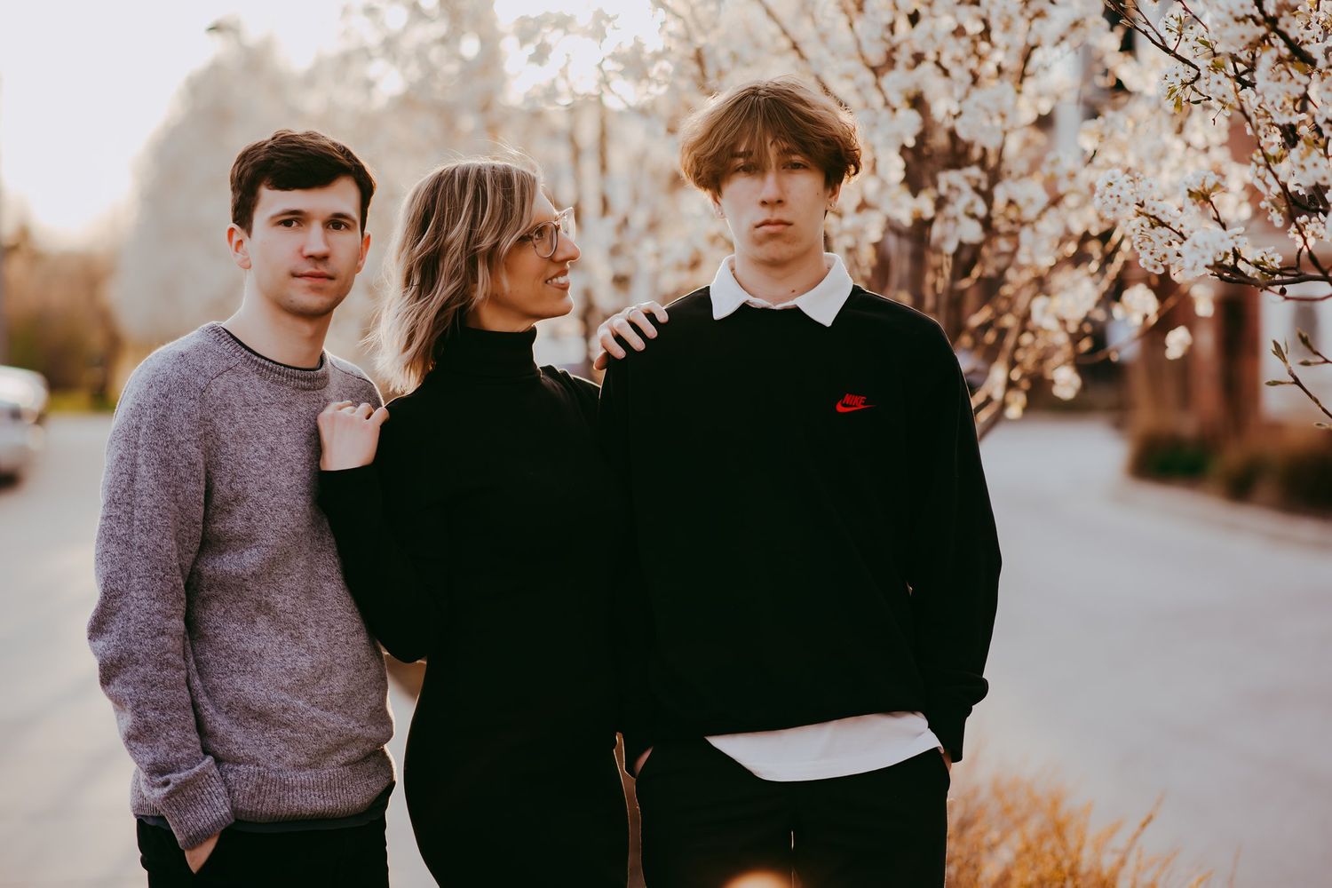 Three people pose together outdoors during sunset with blossoming trees in background.