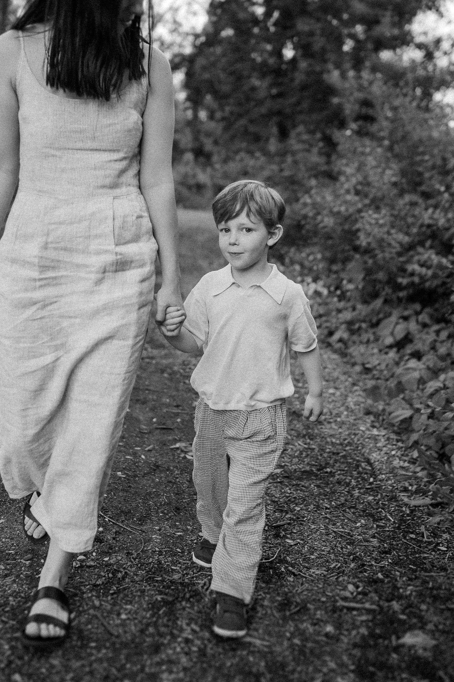 A series of black and white photos showing a small child holding hands while walking down a forest path.