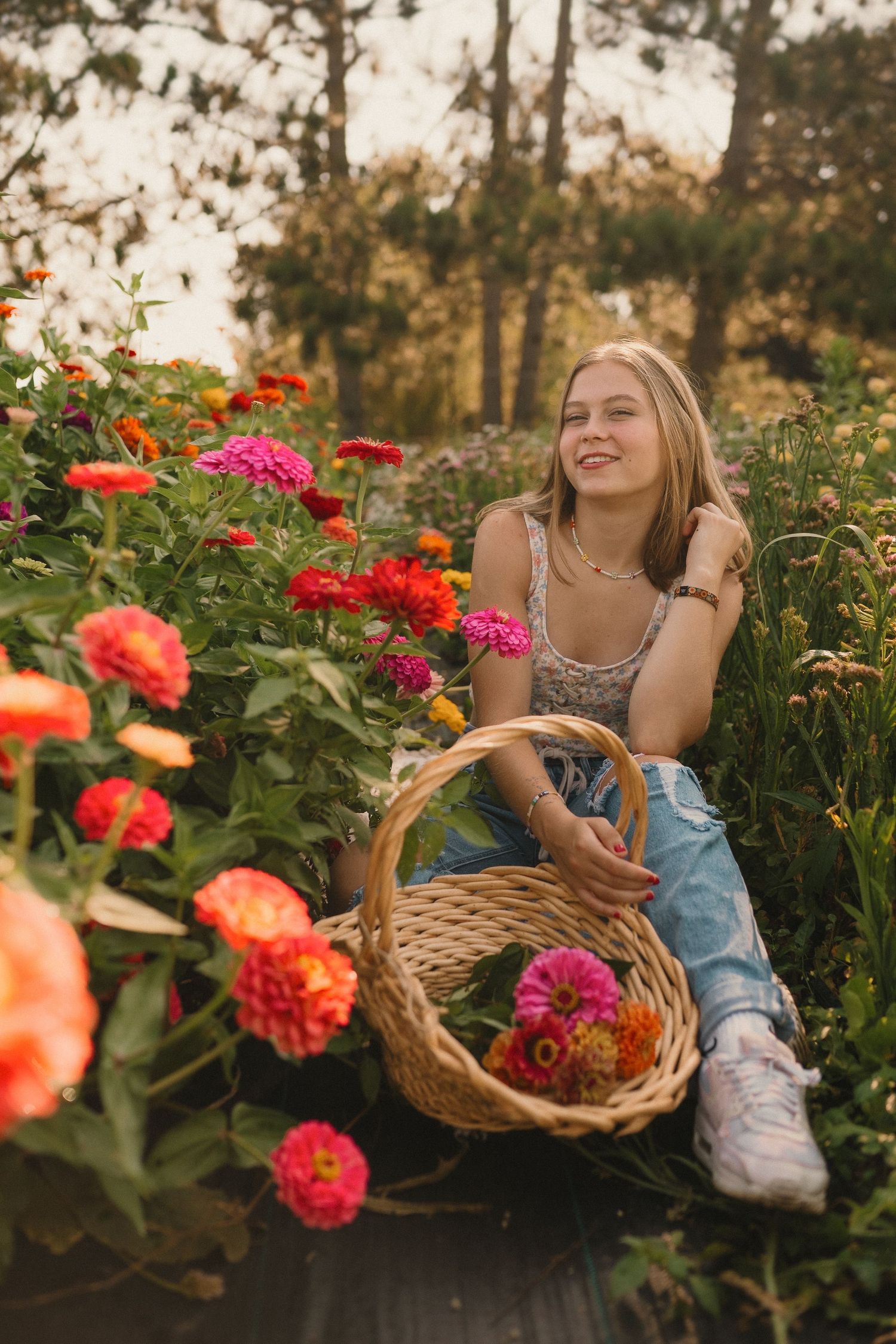 Person sitting in flower garden with wicker basket surrounded by pink and orange blooms at sunset.