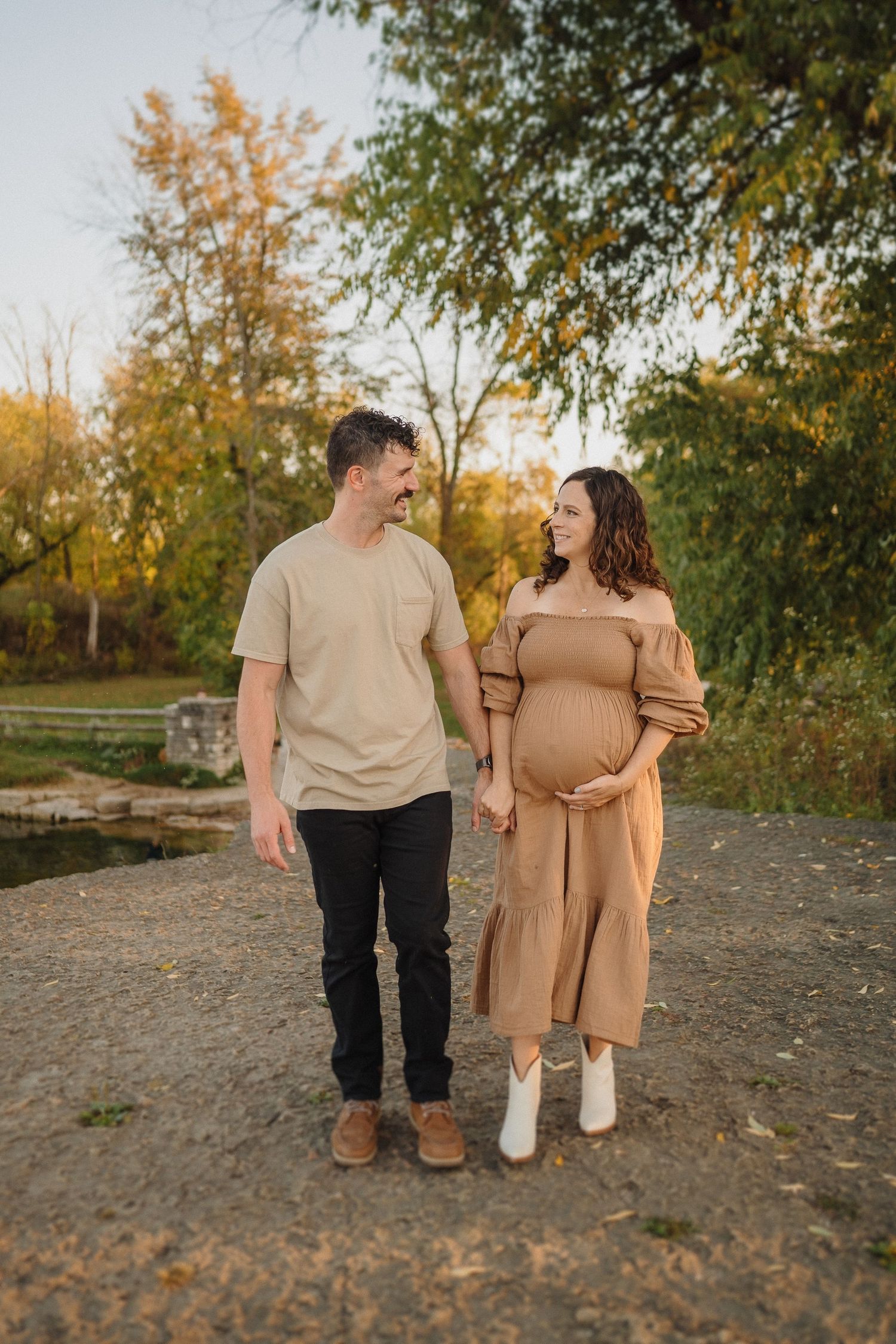 Couple in casual attire takes a romantic autumn stroll with expecting mother wearing a tan dress.