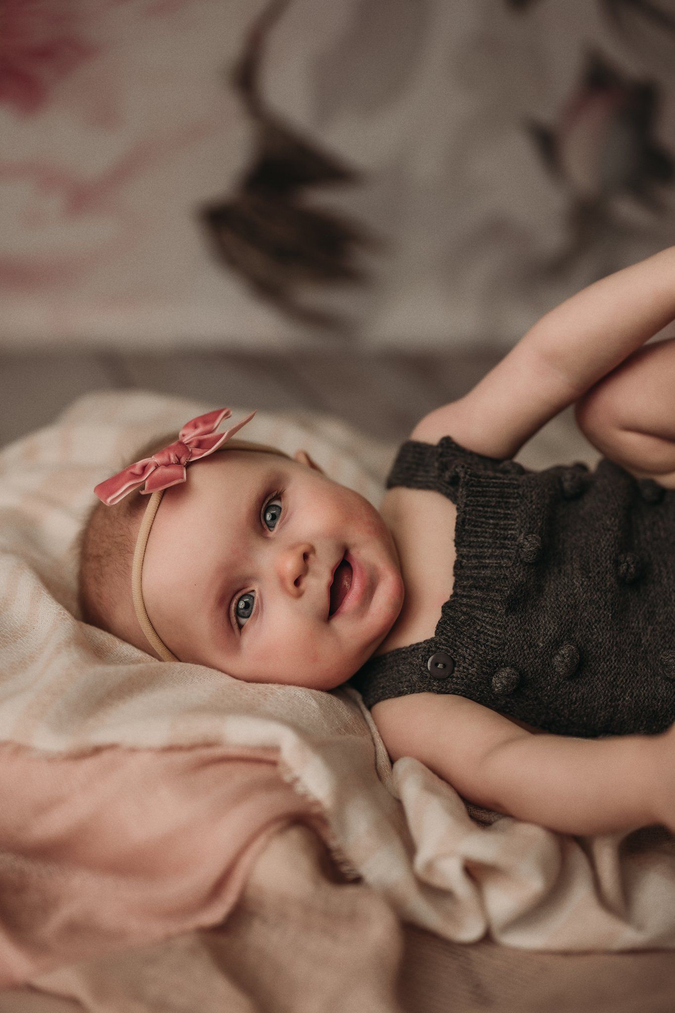 Baby lying on soft pink fabric wearing dark romper and headband.