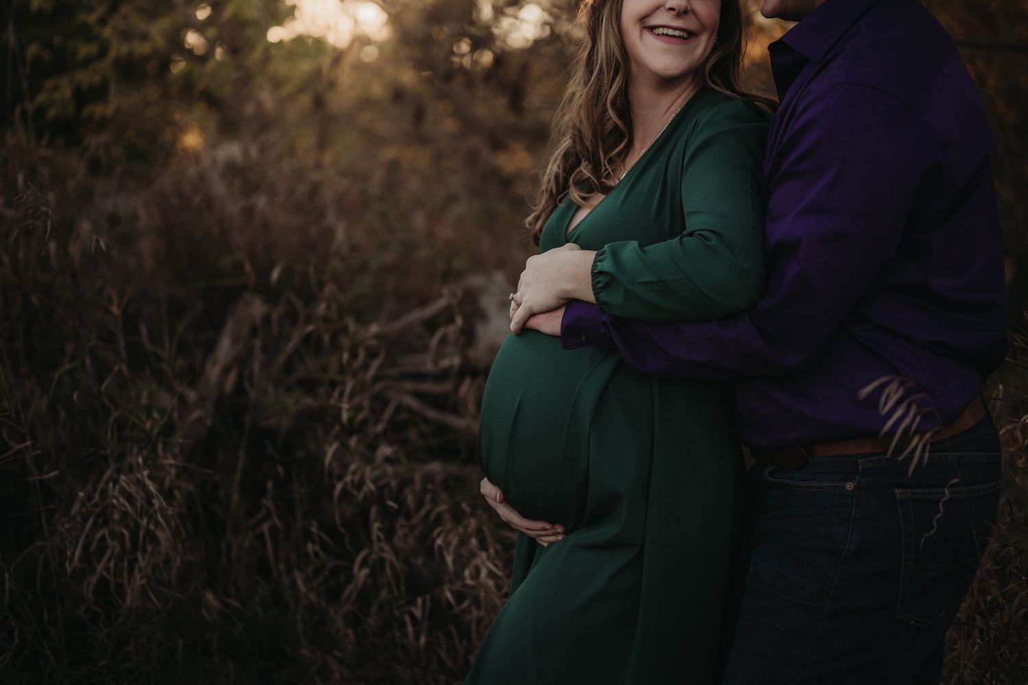 A couple embracing during their maternity photoshoot in natural outdoor setting.