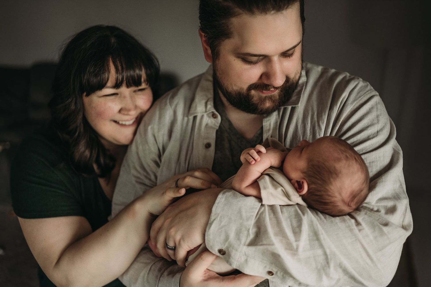 A couple shares a joyful moment while holding their newborn baby.
