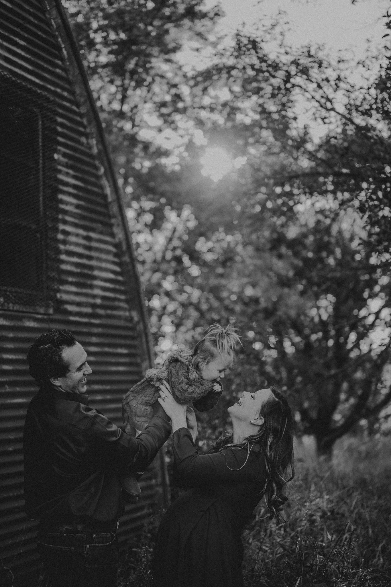 Family sharing a joyful moment together against rustic barn wall at sunset.
