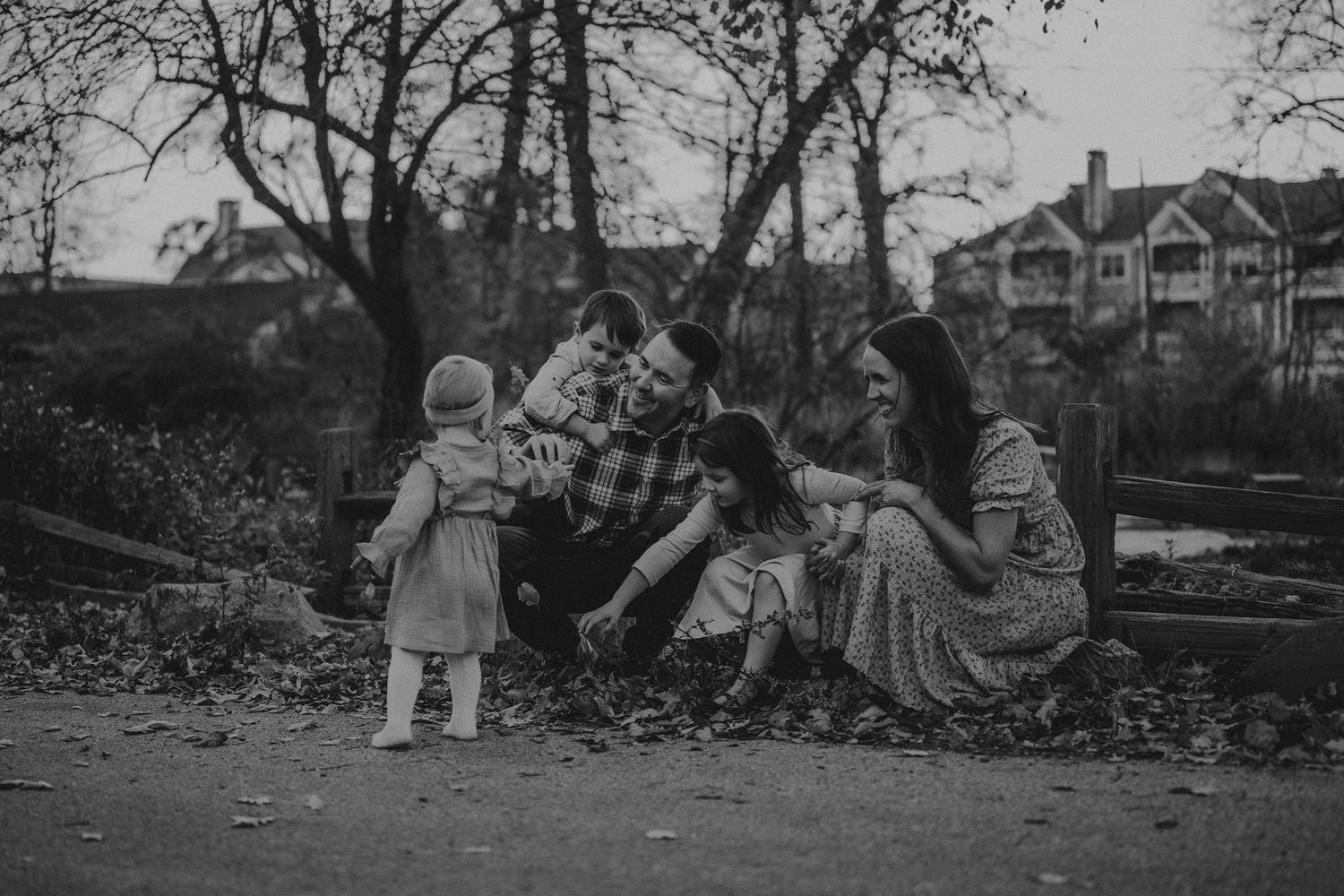 A black and white photo captures a candid family moment outdoors in autumn.