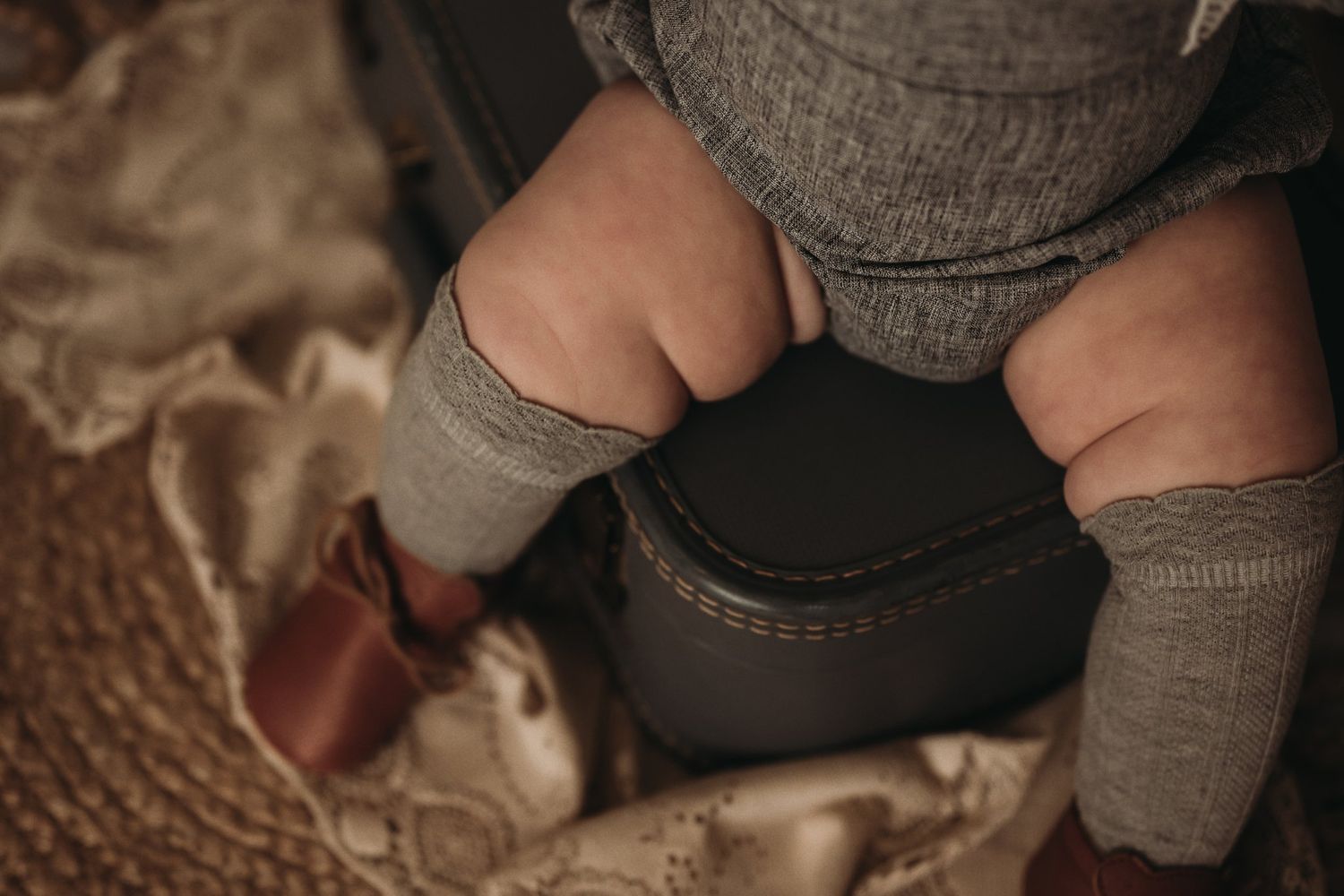 Close-up detail of small feet in gray socks against a textured beige fabric background.