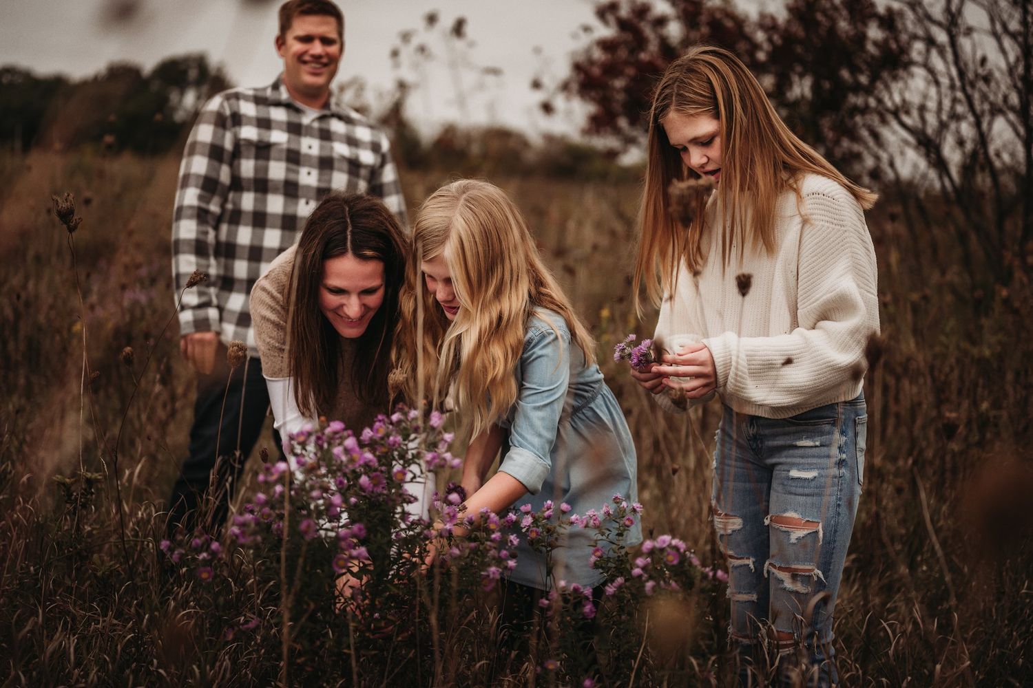 Family exploring purple wildflowers in an autumn field during golden hour.