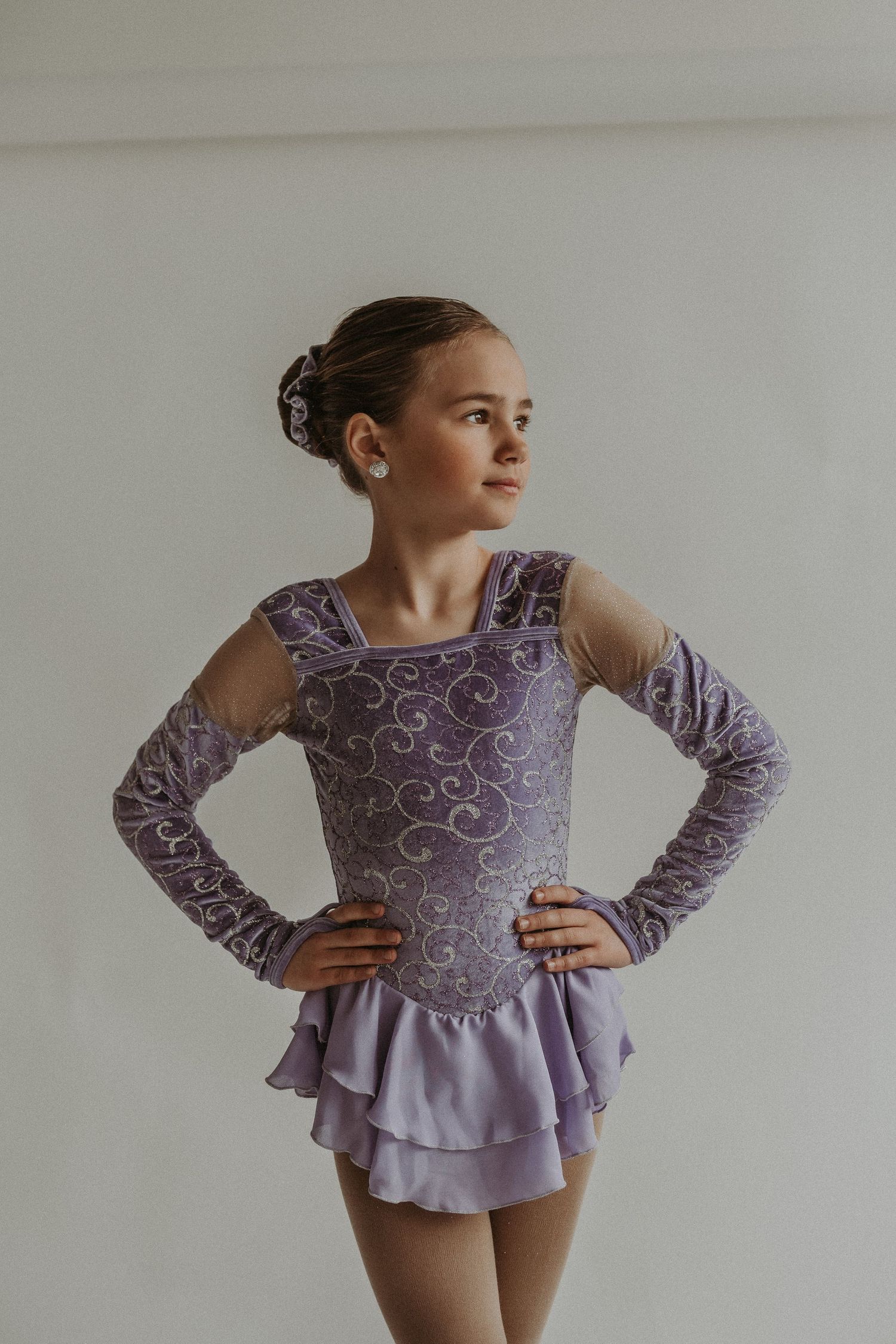 Ice skater poses confidently in sparkly purple performance dress against white background.