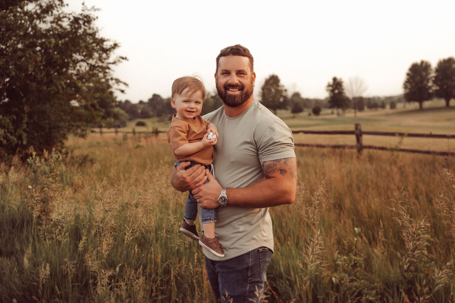 Warm sunset portrait of family members sharing a happy moment in a rural field with wooden fencing.
