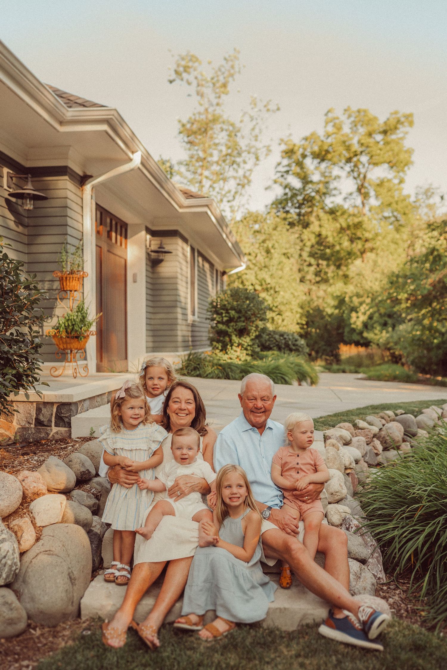 Family members sitting together on decorative rock landscaping in front of a grey house at sunset.
