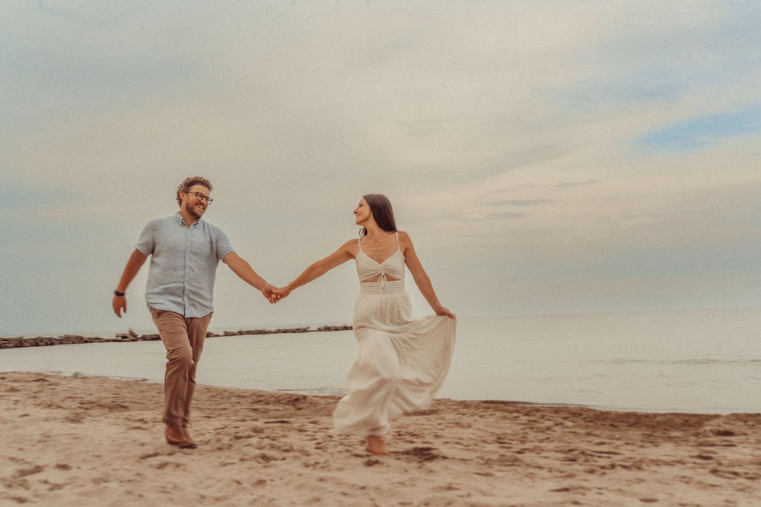 Romantic couple runs playfully on beach holding hands at sunset.