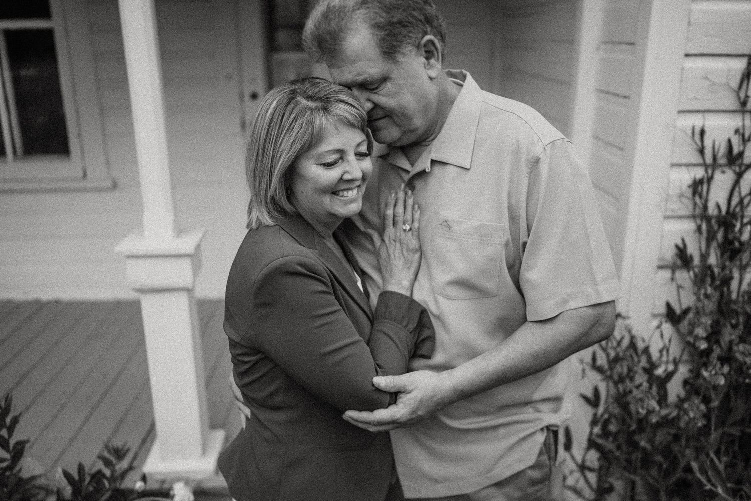 Black and white intimate portrait of couple embracing on farmhouse porch.