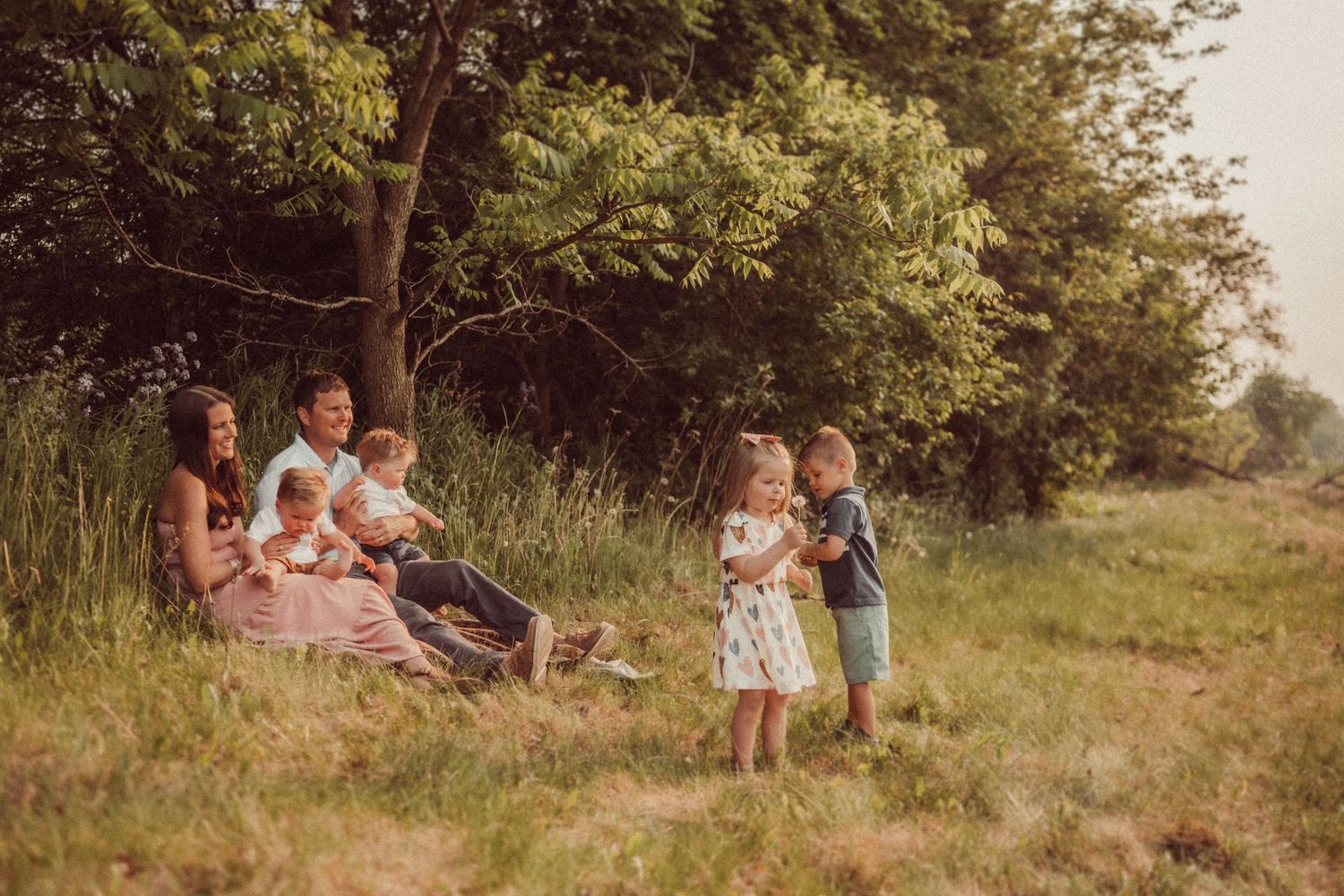 Vintage photo of family picnic gathering in grassy field near trees.