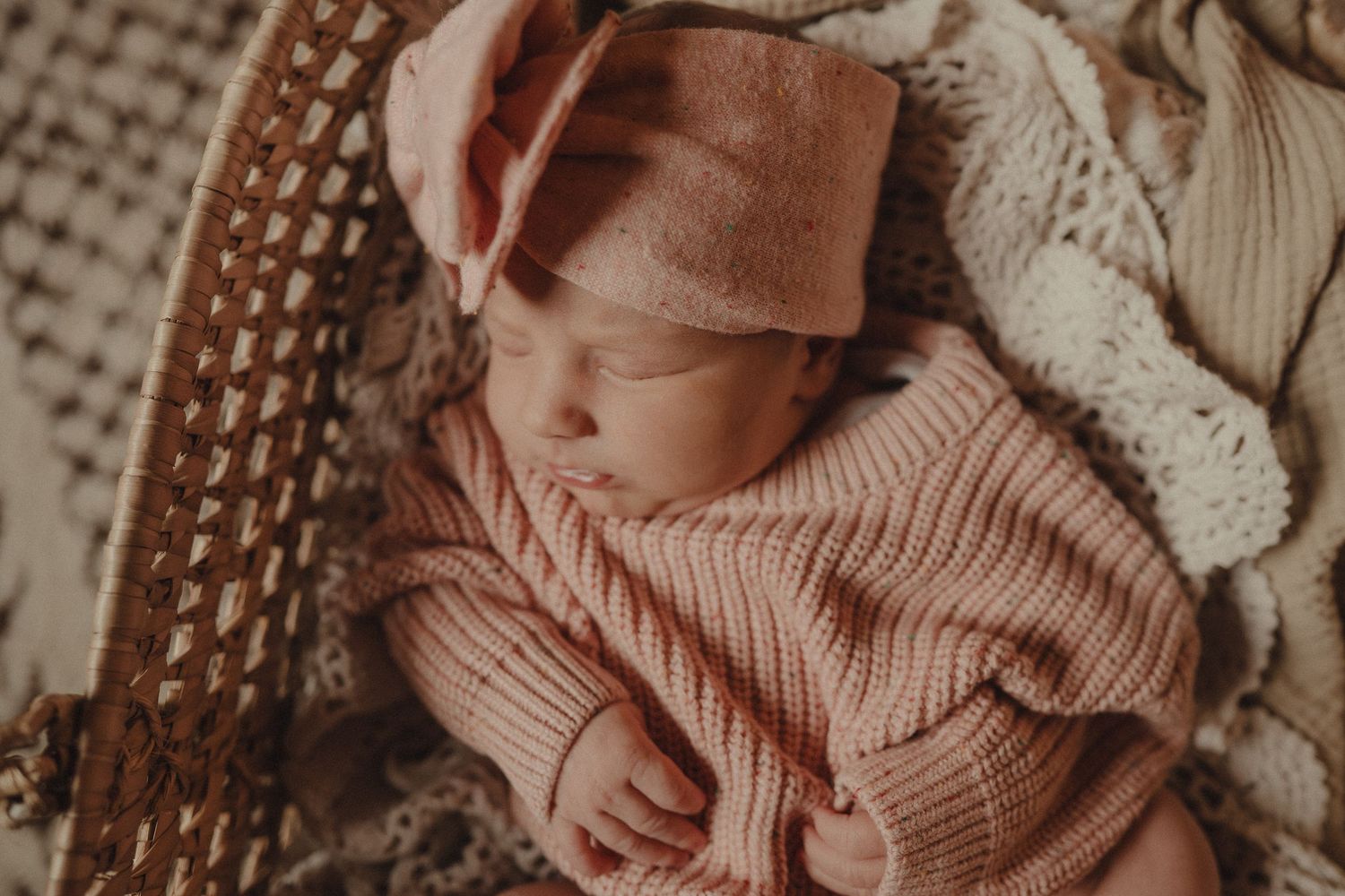 A baby in a cozy knit sweater lies on a textured blanket in warm sepia tones.