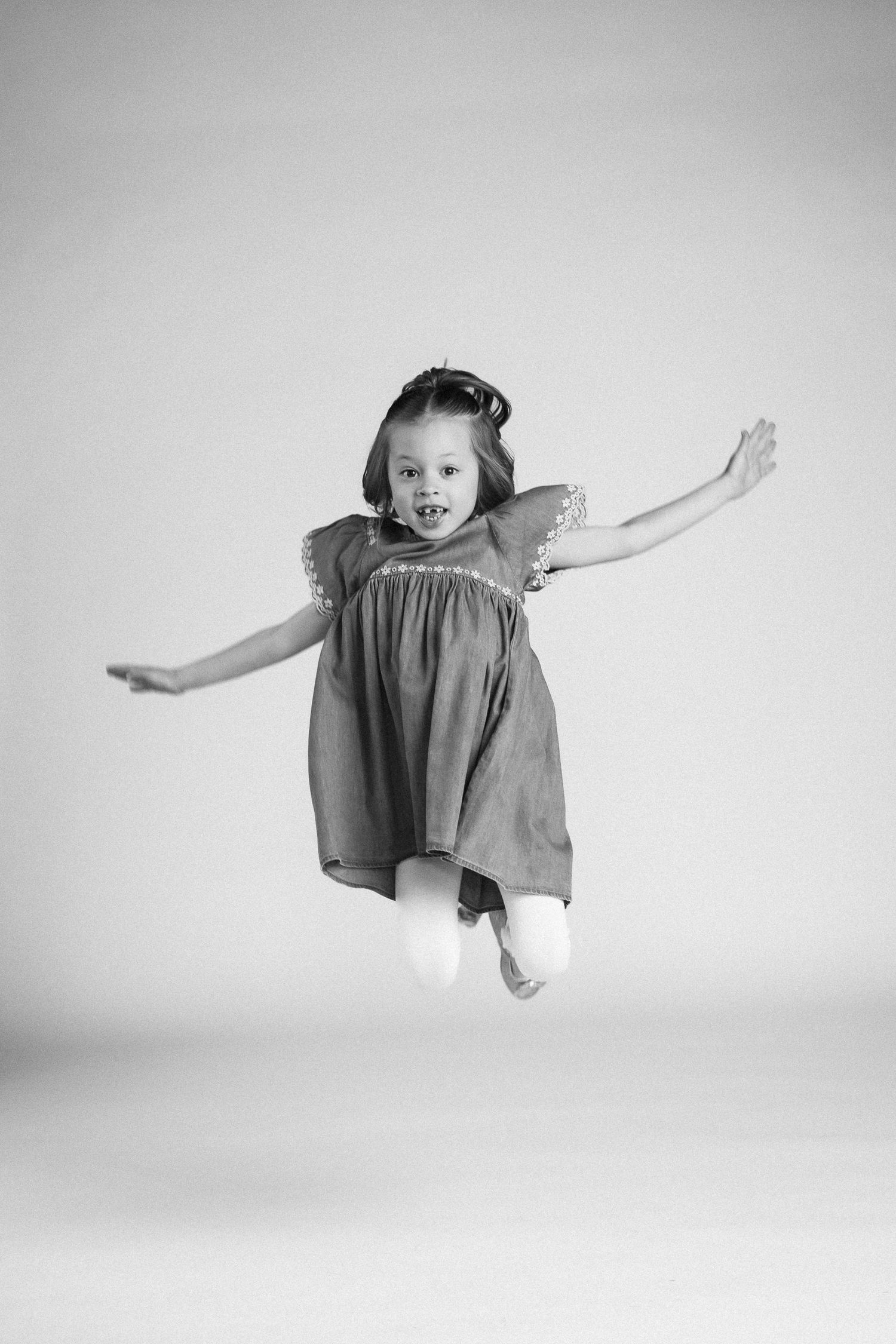 A sequence of black and white photos showing a young child in a dress making joyful leaping movements through the air.