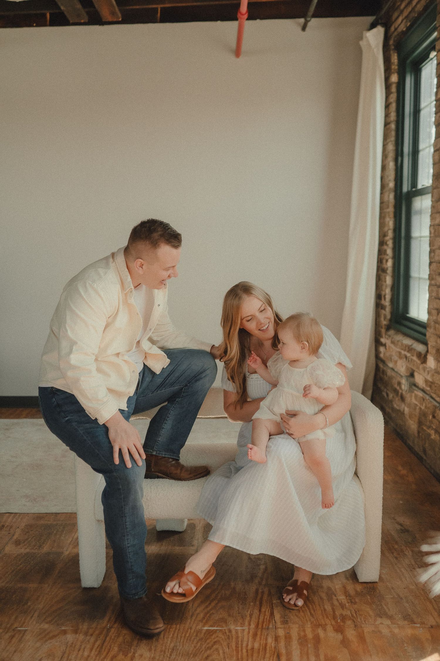 Family of three sharing a joyful moment together in a bright studio with brick accent wall.