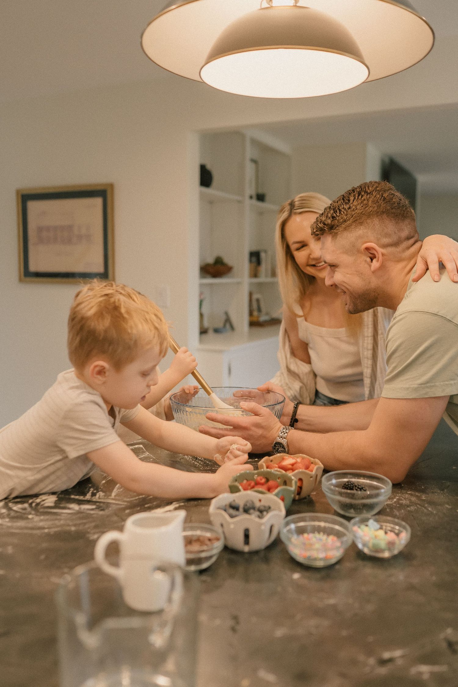 A happy family with a young boy bakes together at a kitchen counter with colorful ingredient bowls.